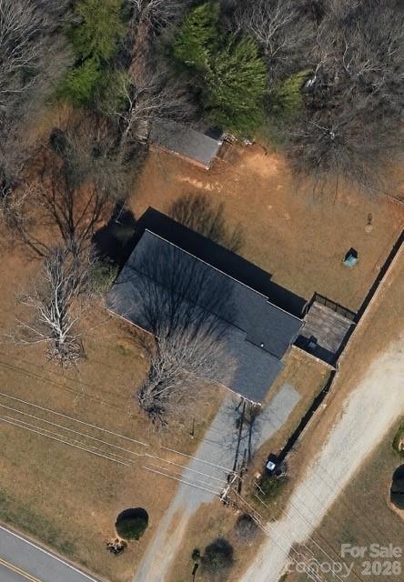 Aerial view of a dark-roofed house surrounded by a yard and leafless trees beside a road.