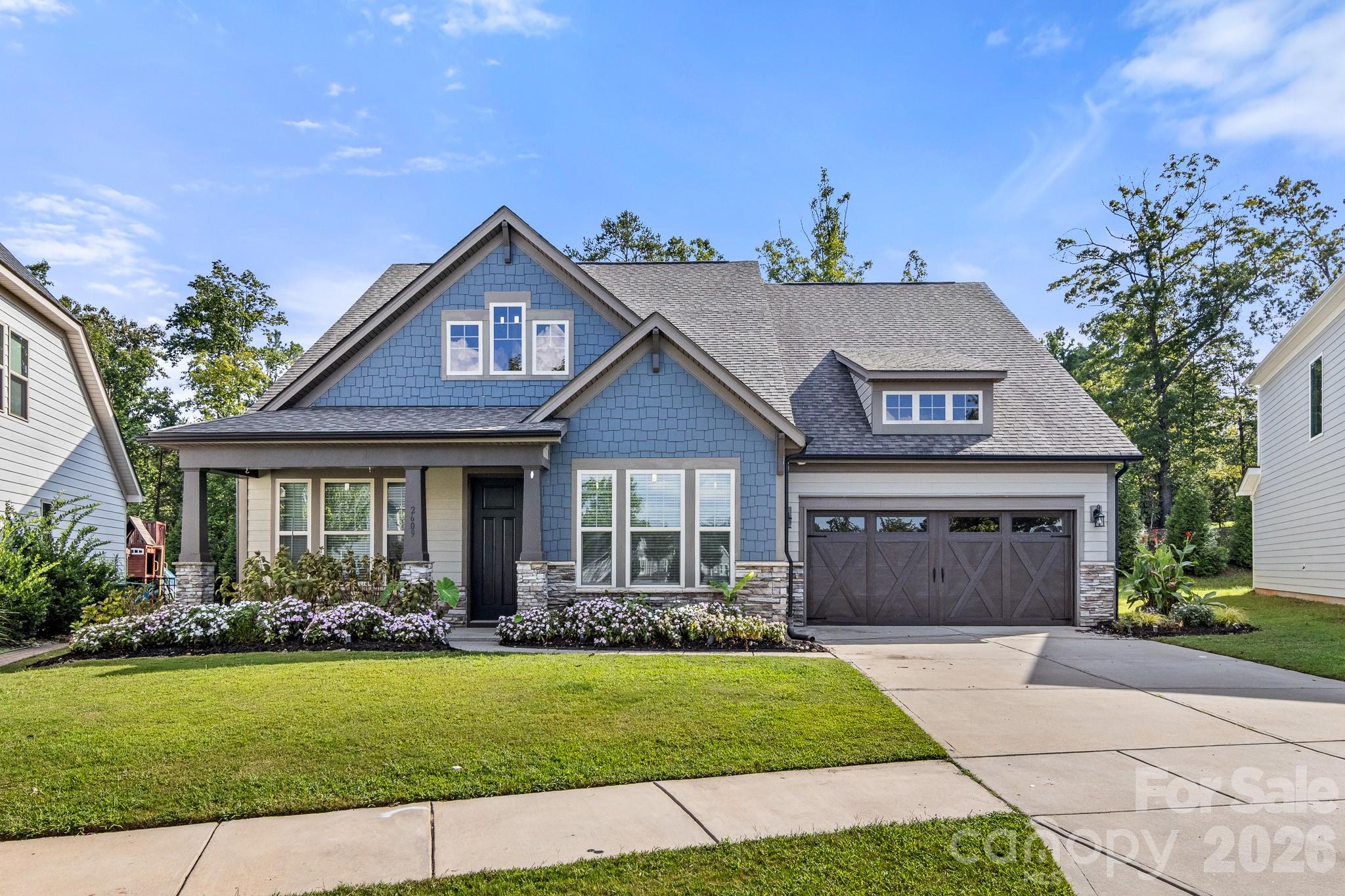 Blue-shingle home with a covered porch, dark double garage door, and landscaped front lawn.