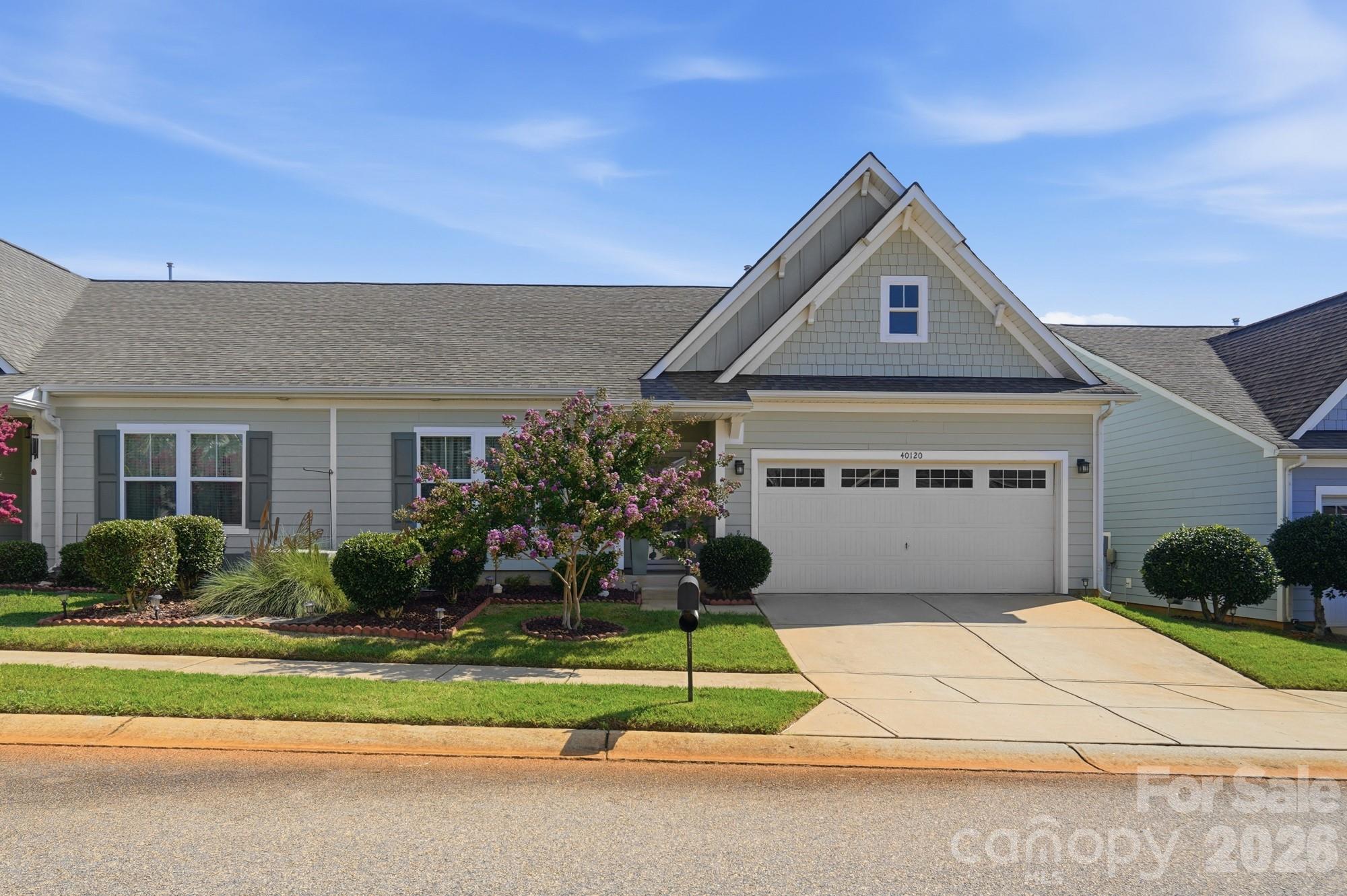 Gray-sided home with a steep front gable, two-car garage, and flowering landscaping.