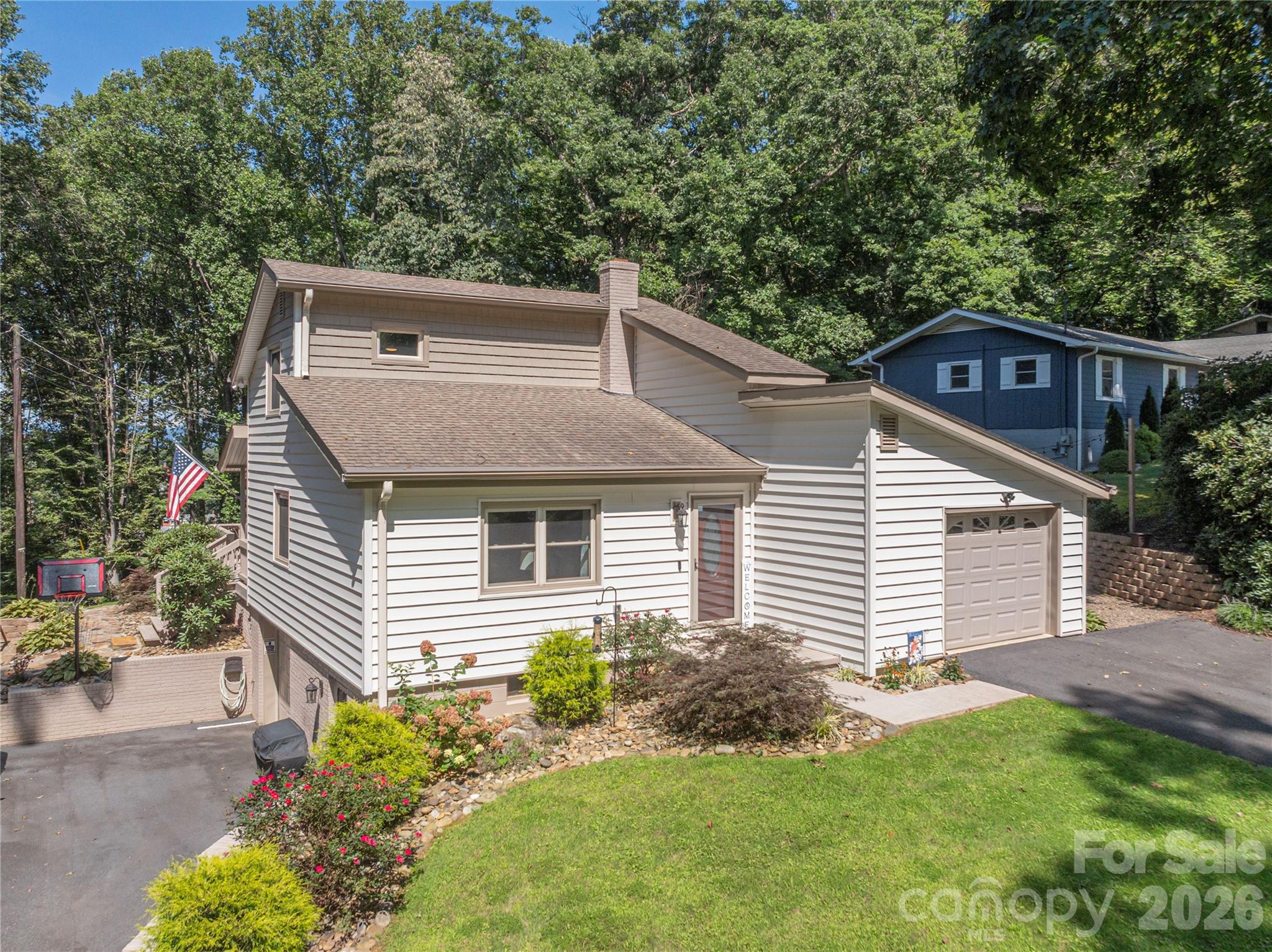 Split-level home with an attached garage, landscaped lawn, and wooded surroundings.