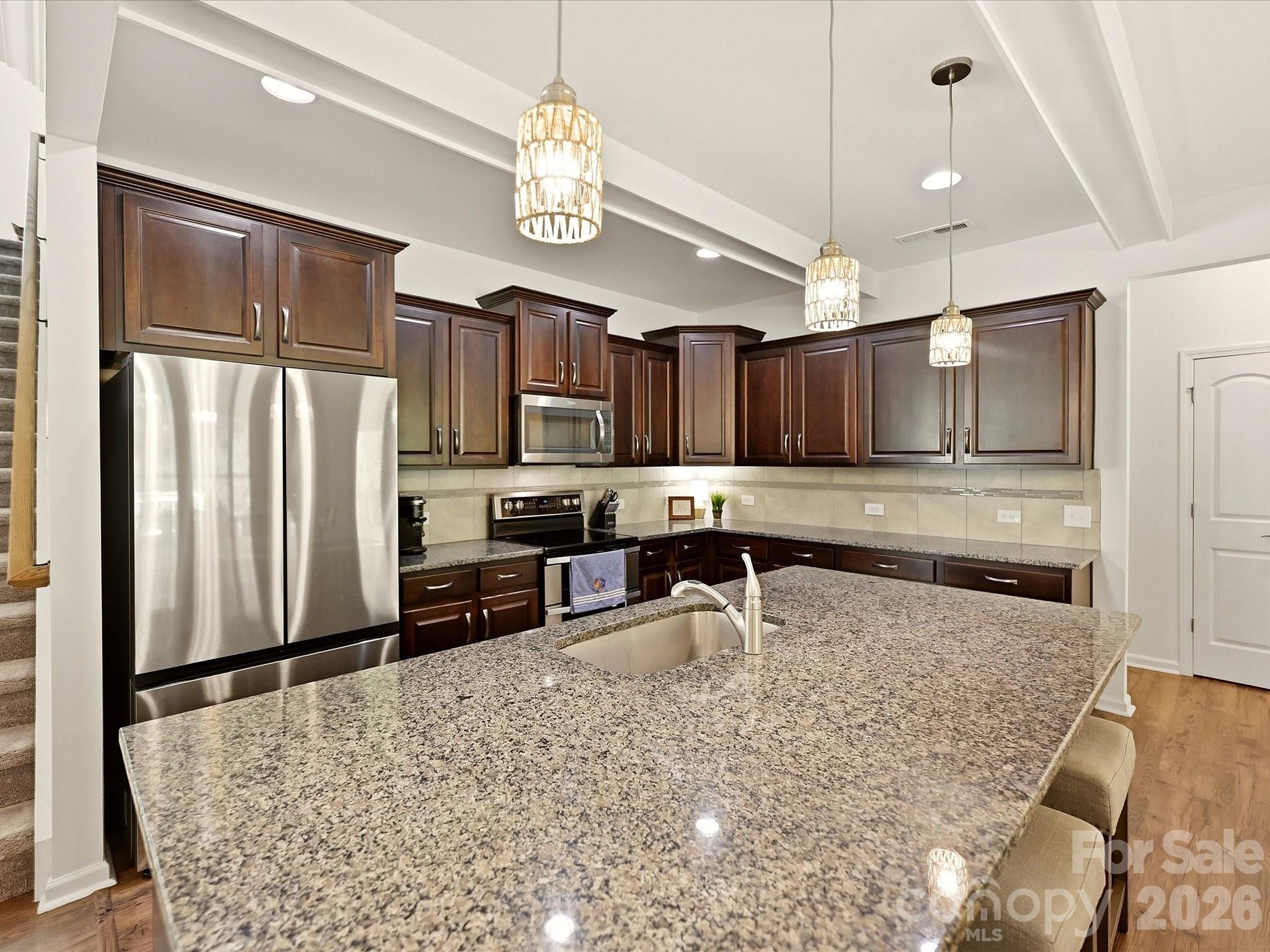 Kitchen with dark cherry cabinets, stainless steel appliances, and a large granite island.