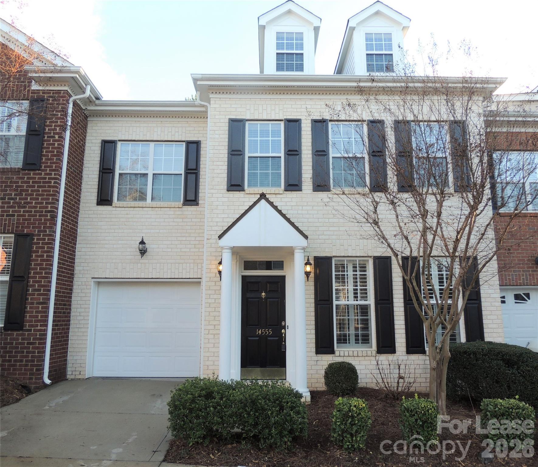 Cream brick two-story house with dark shutters, a white garage door, and a columned entry.
