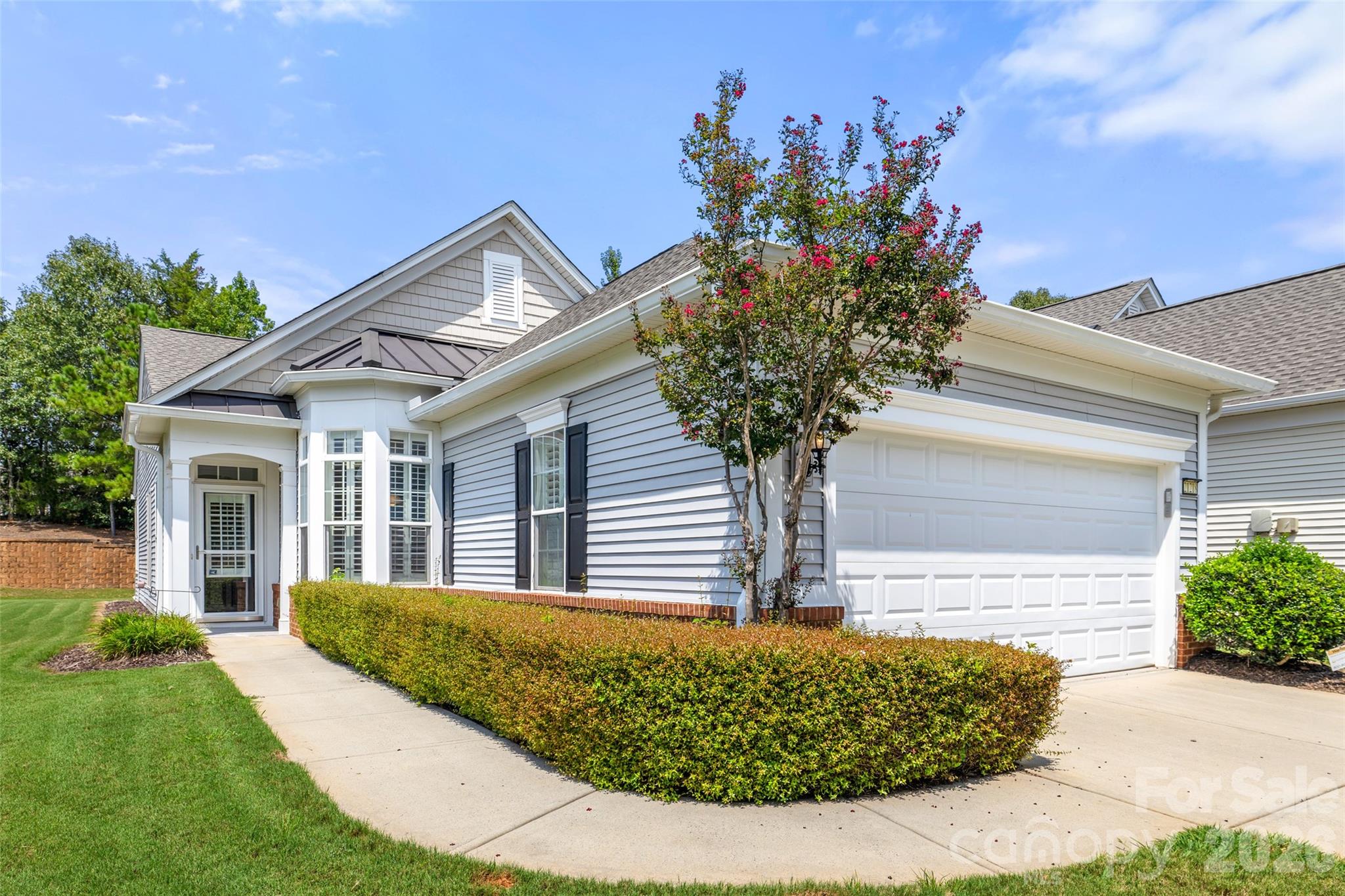 Gray-sided home with an attached garage and a flowering tree in front.