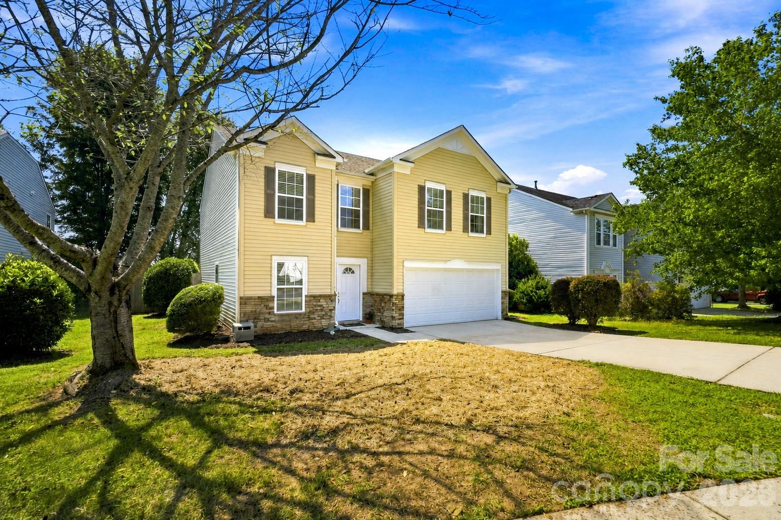 Two-story yellow house with stone veneer, an attached double garage, and a landscaped front yard.