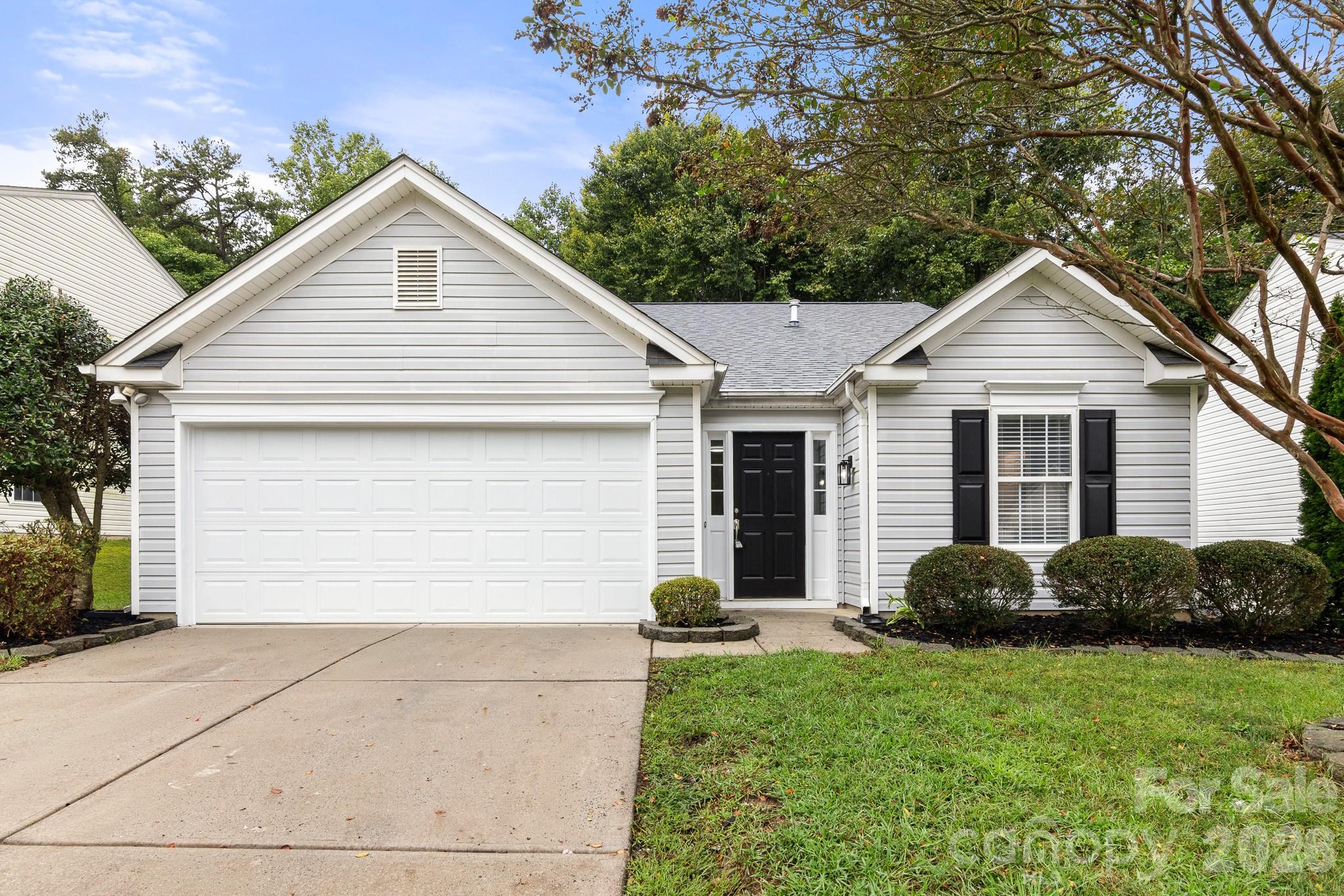 Light gray house with a large white garage, black front door, and landscaped shrubs.