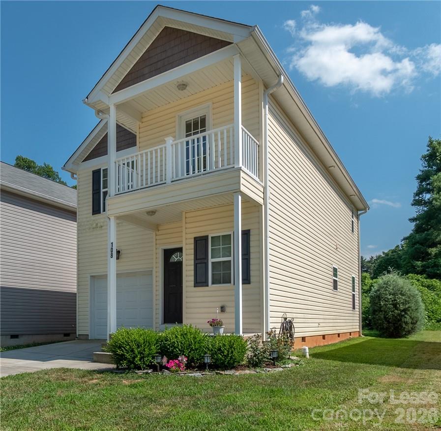 Two-story pale yellow house with a covered balcony, attached garage, and landscaped front garden.