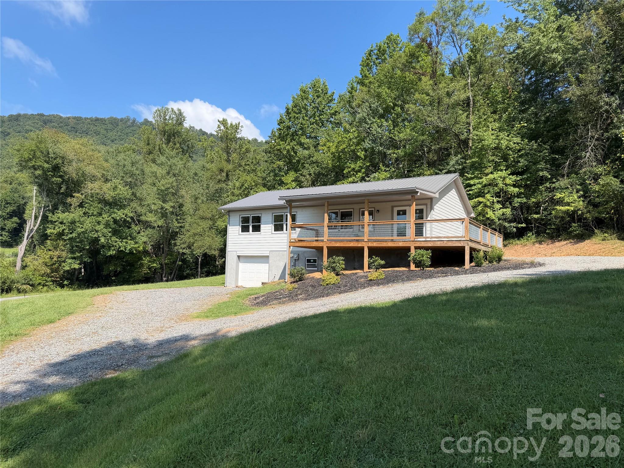 Home with a raised wooden deck and gravel driveway, surrounded by trees on a wooded hillside.