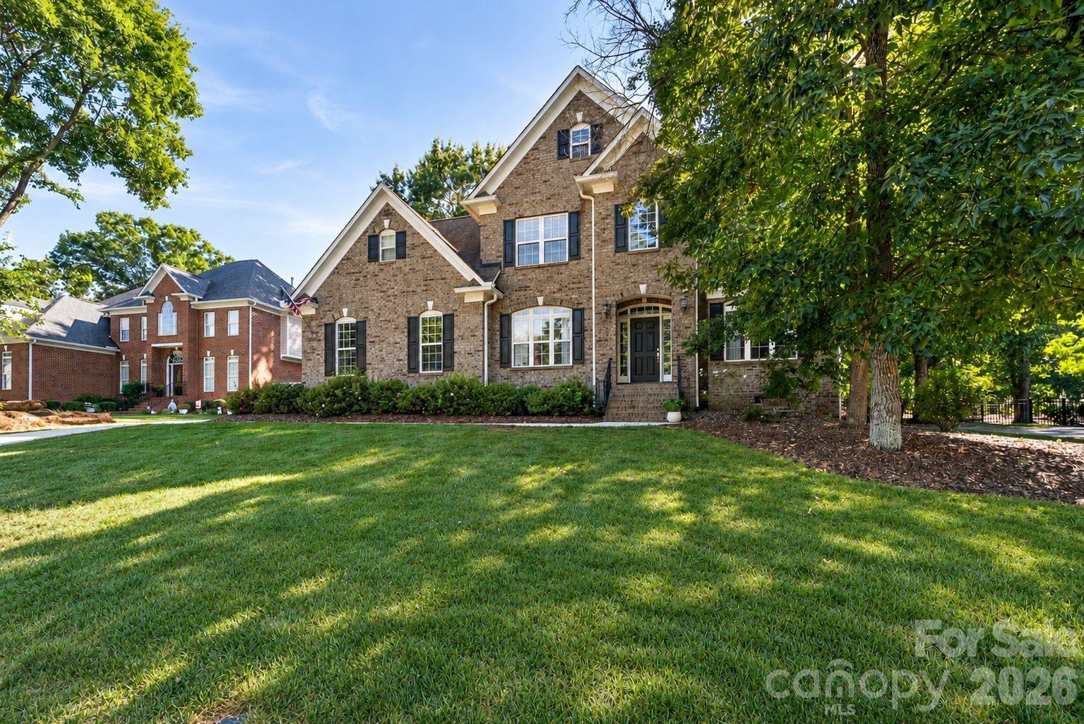 Two-story stone house with steep gables, dark shutters, and a broad tree-shaded lawn.