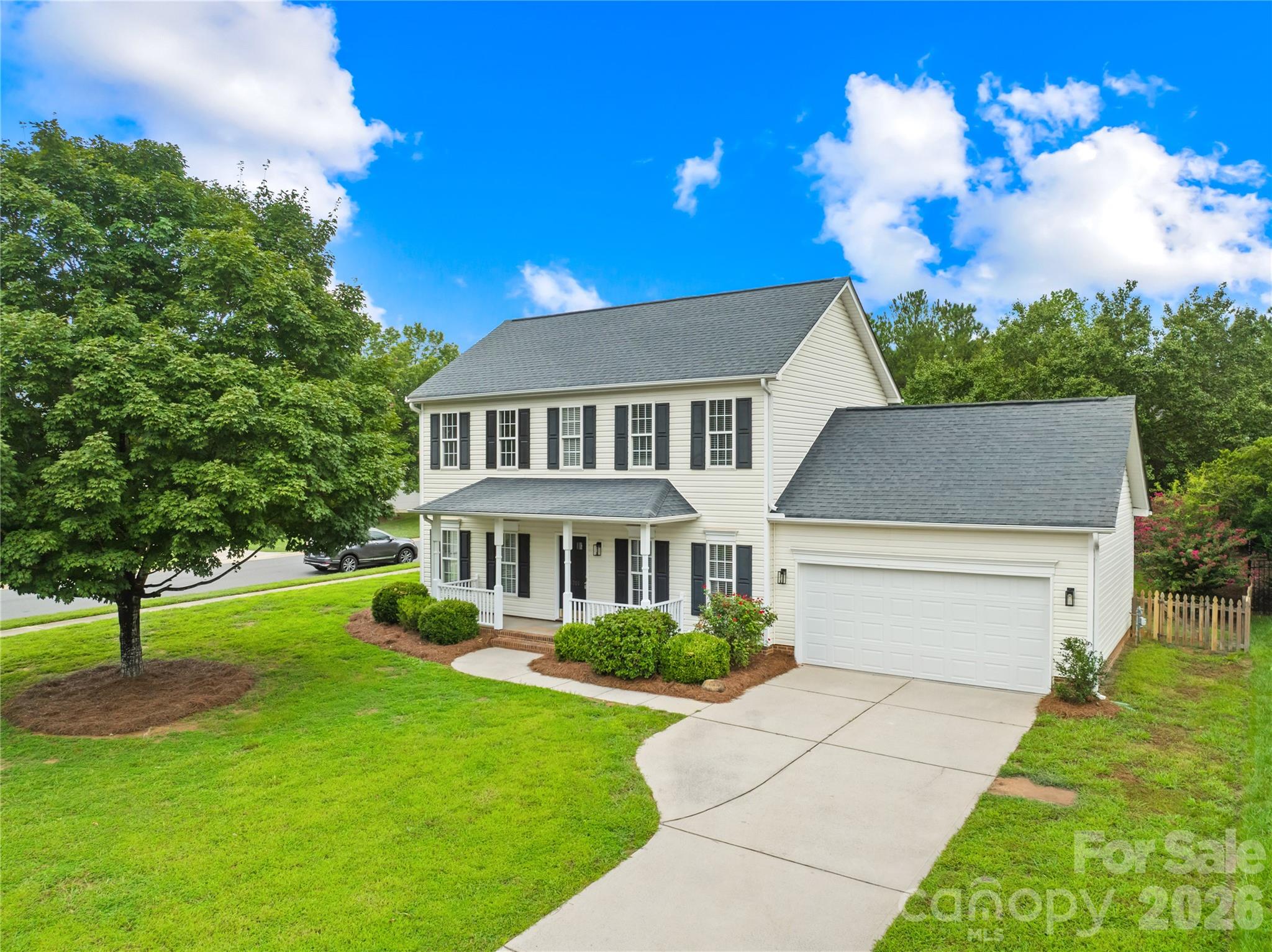 Two-story white house with dark shutters, attached garage, covered porch, and broad front lawn.