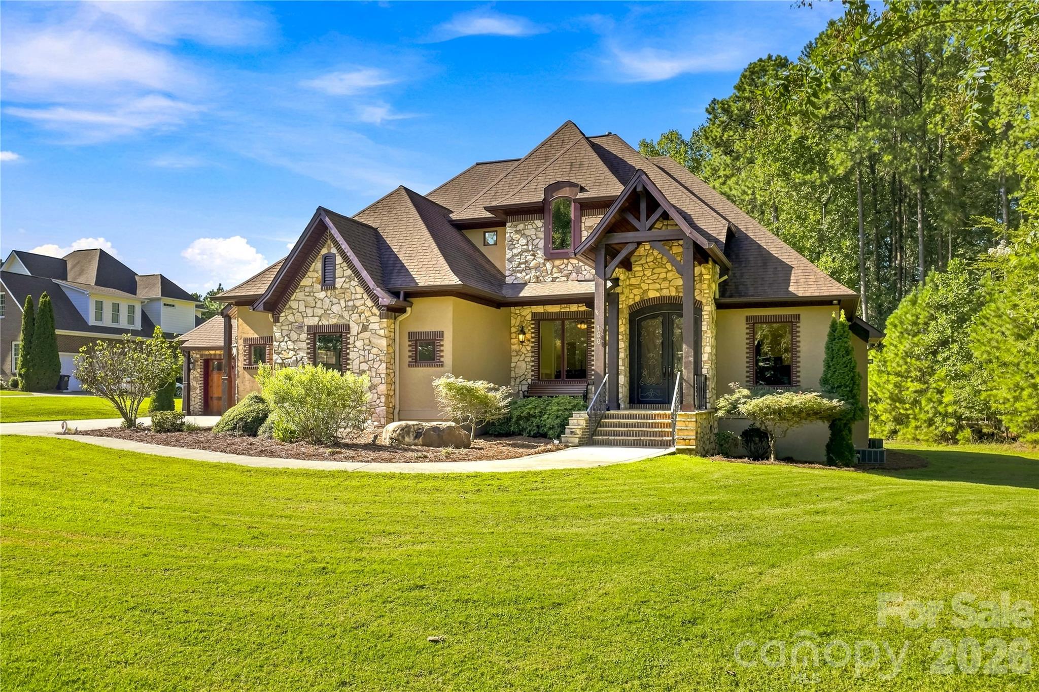 Stone-and-tan two-story home with a timber-framed entrance, landscaped shrubs, and broad green lawn.