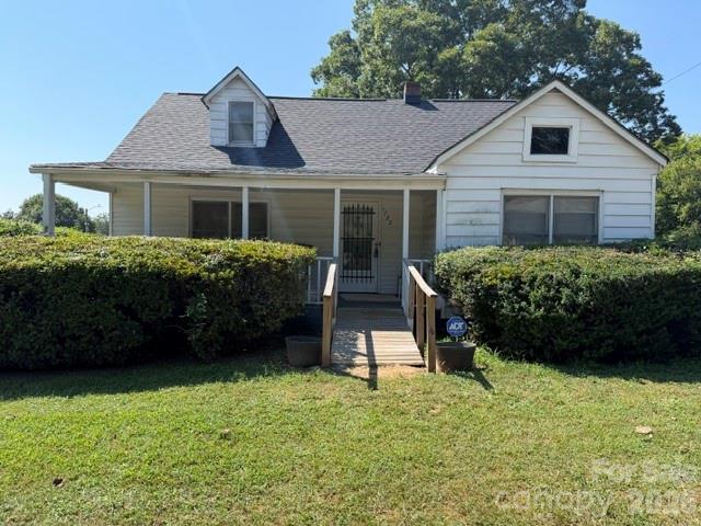 White single-story house with a covered porch, wooden entrance steps, and hedges along the front yard.
