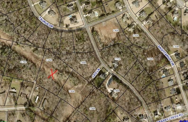 Aerial parcel map with a red X marking a wooded lot among labeled roads and property boundaries.