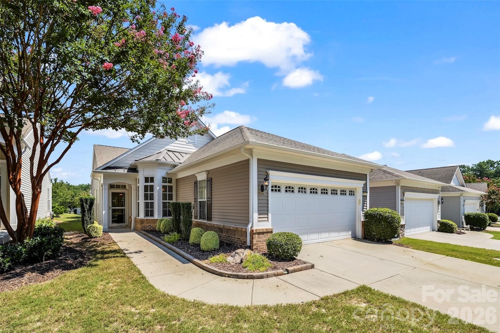 Front exterior of a beige-sided home with a white double garage and landscaped entry.