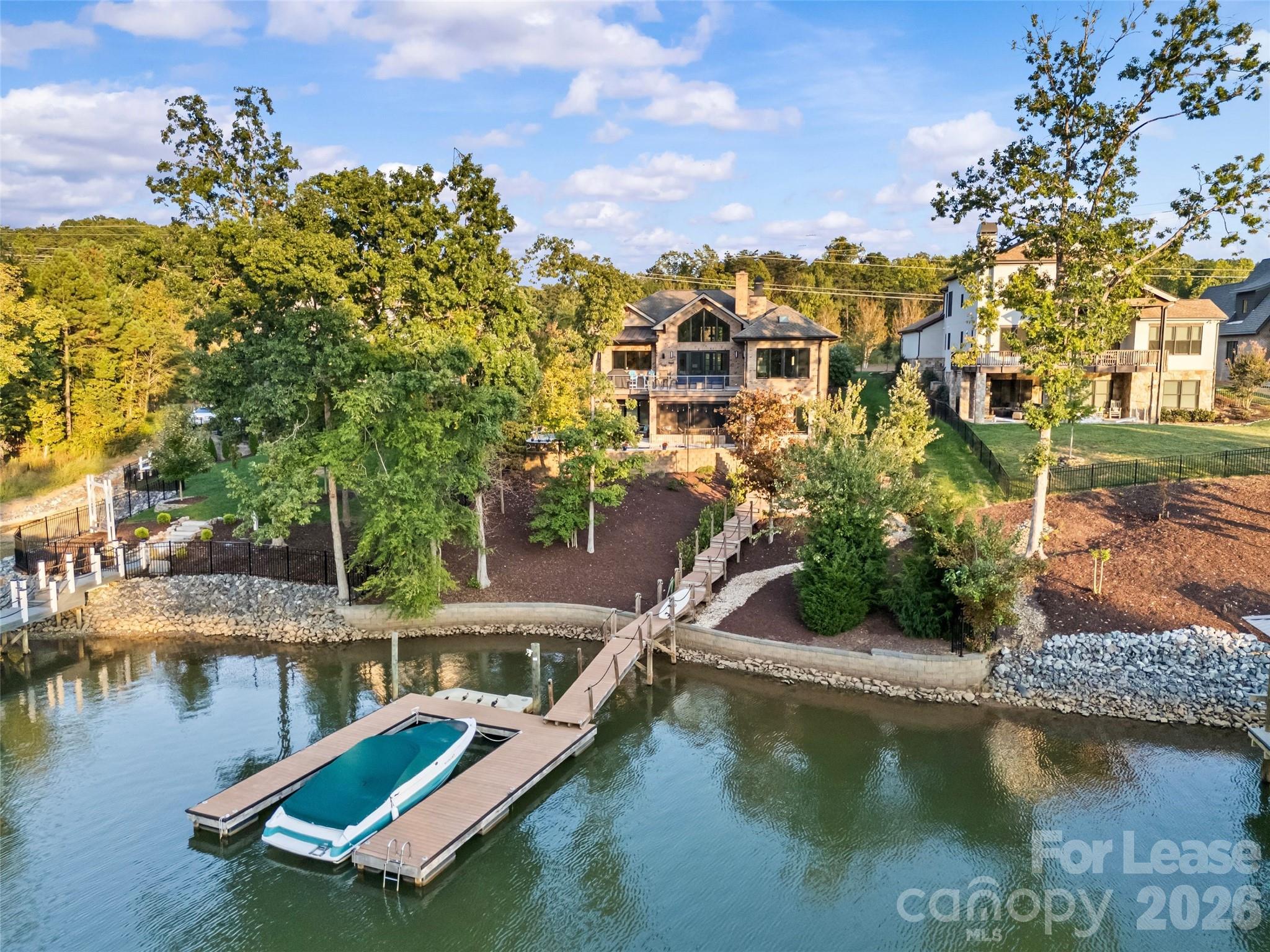 Waterfront home with landscaped yard, long dock, and covered boat at the water’s edge.