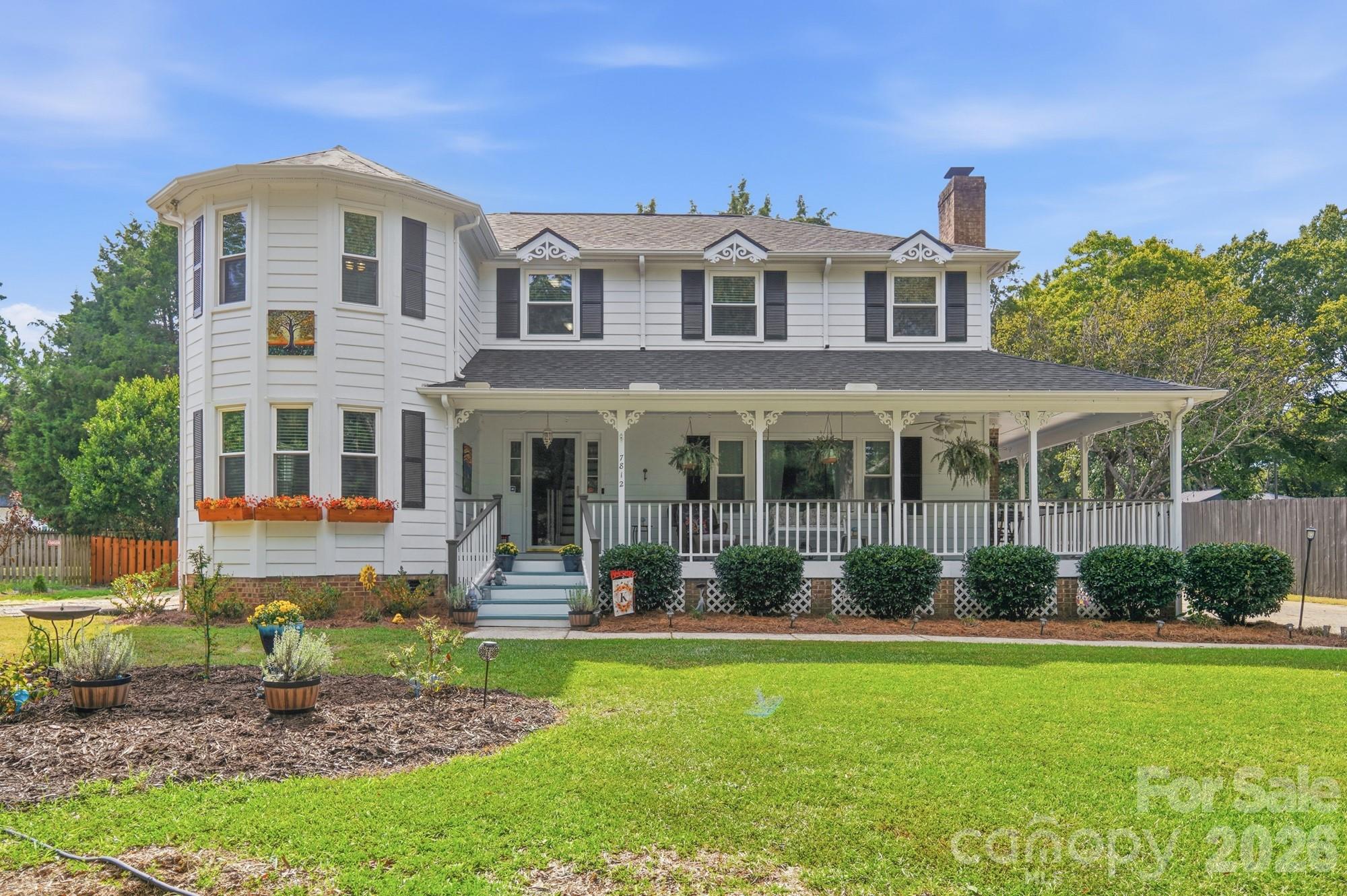 White two-story house with a wraparound porch, flower boxes, and a broad green lawn.