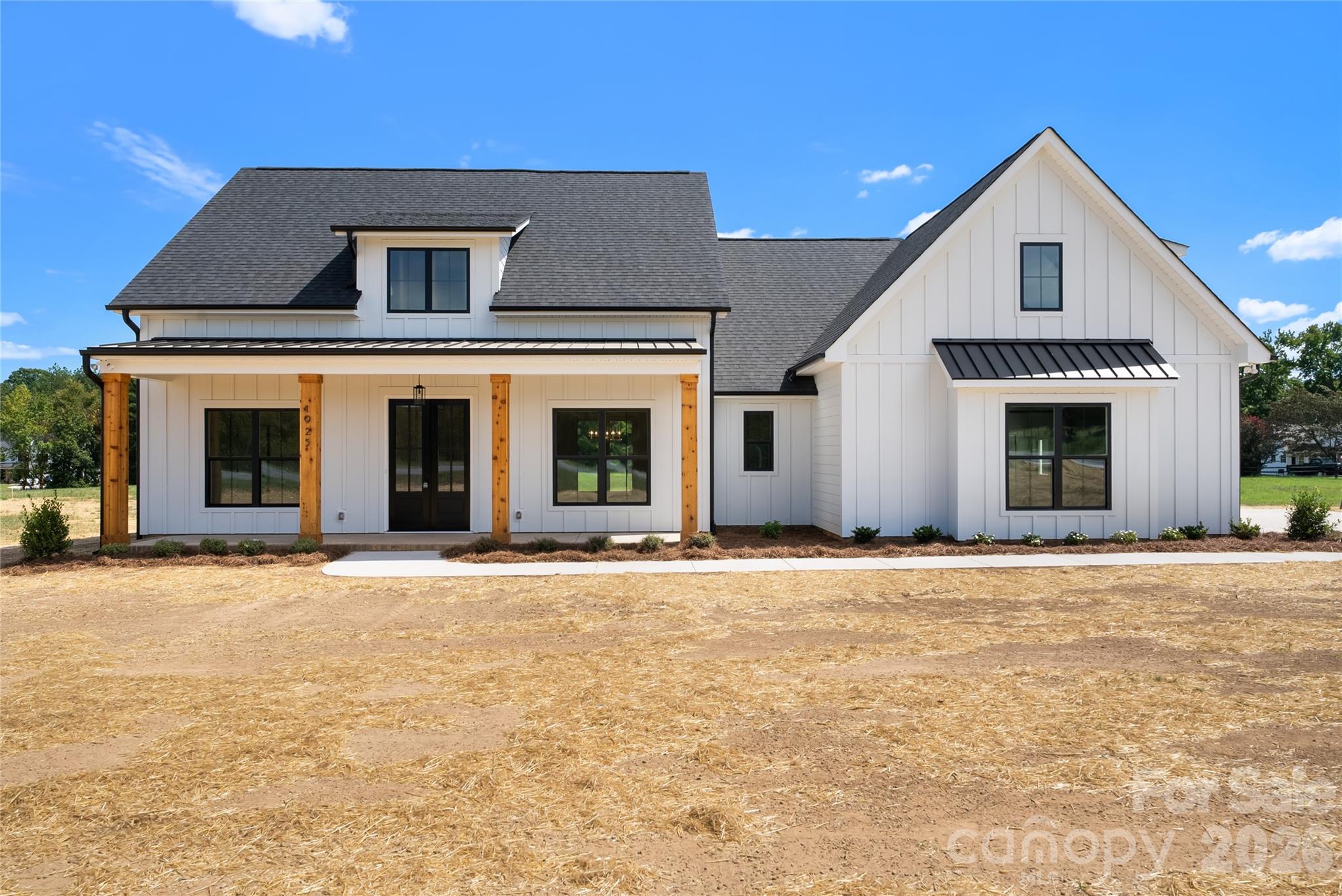 White farmhouse with dark roofs, black-framed windows, and a covered porch with wood posts.