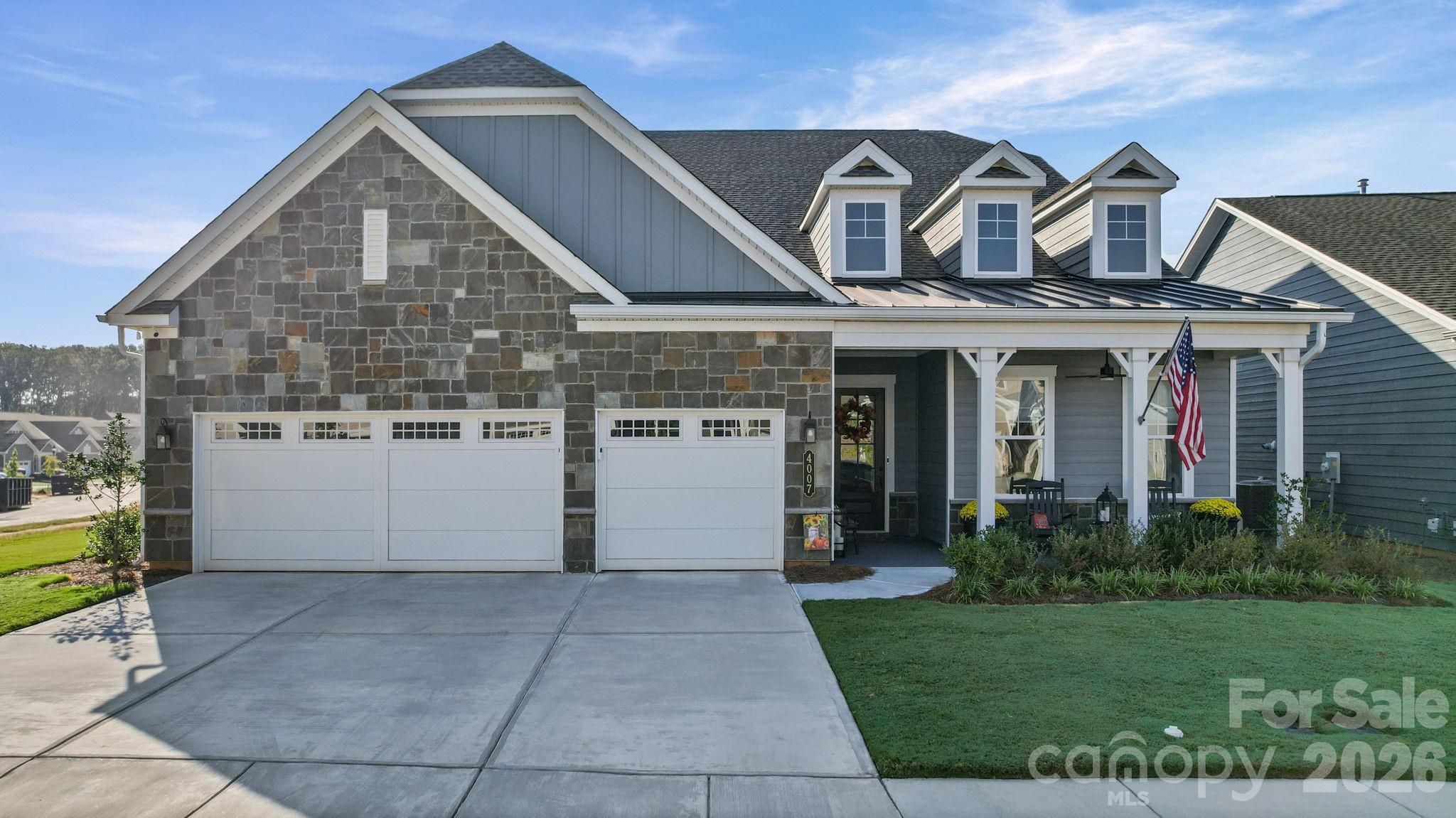 Gray-and-stone house with three garage doors, dormer windows, and a covered porch with an American flag.