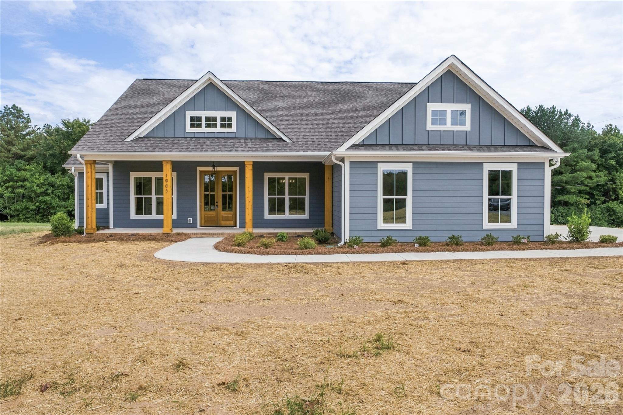 Blue-gray house with a covered wood-post porch, steep gabled roof, and dry front yard.