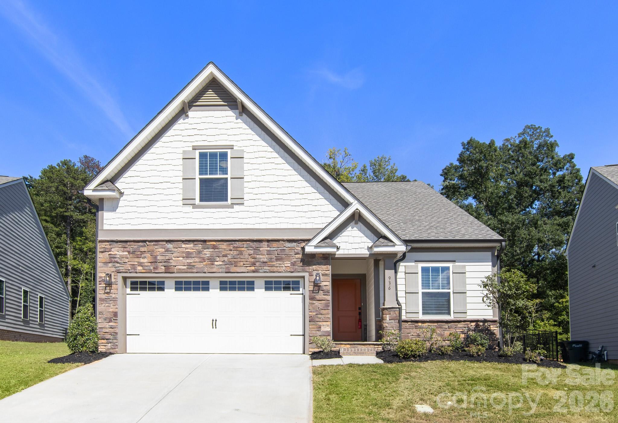 Two-story white-and-stone home with a steep front gable, two-car garage, and wide driveway.
