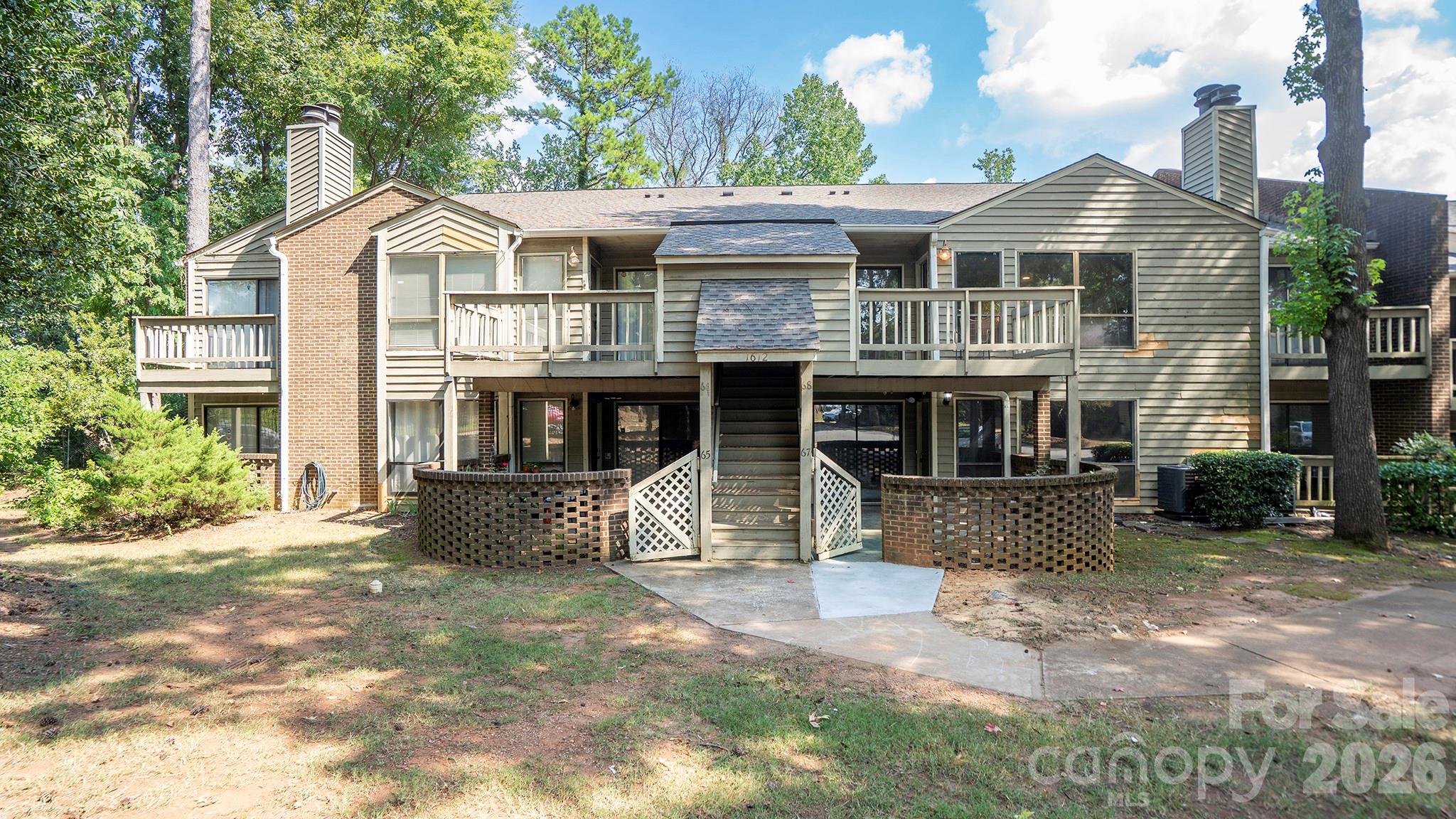 Condominium exterior with multiple balconies and a central staircase, surrounded by mature trees.