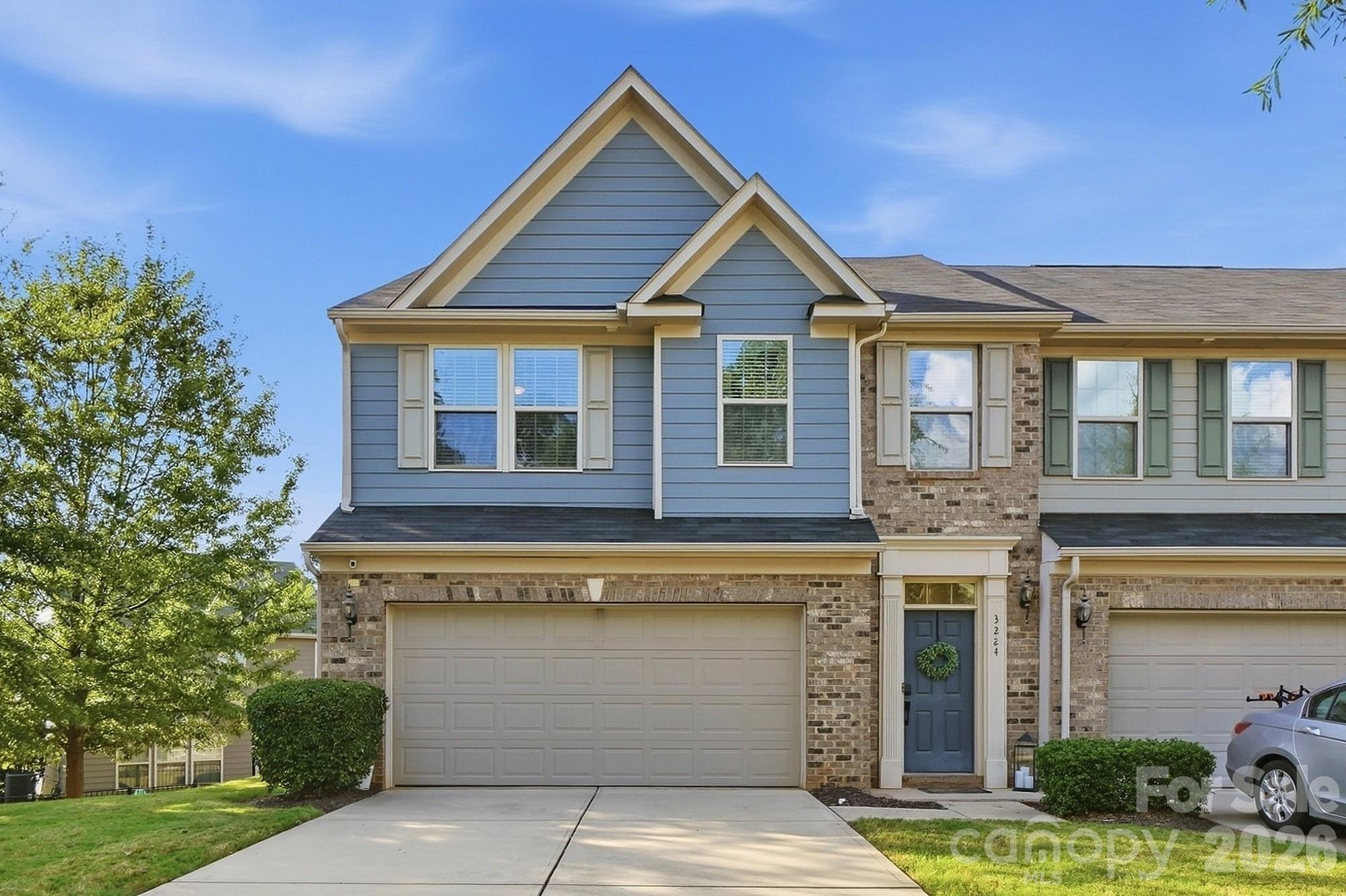 Two-story attached home with blue-gray siding, brick accents, blue entry door, and double garage.
