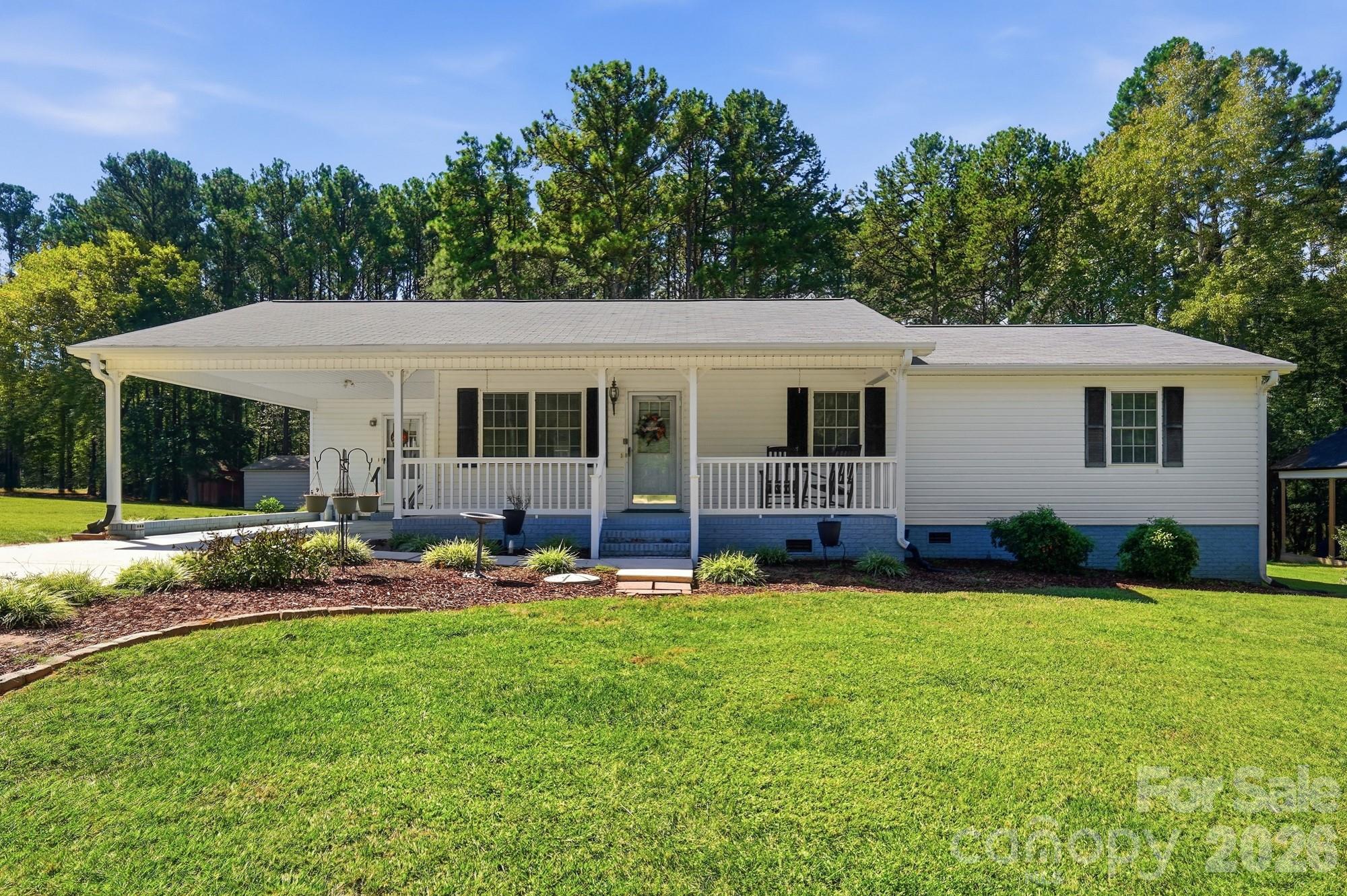 White single-story home with a covered porch, blue brick foundation, and broad green lawn.