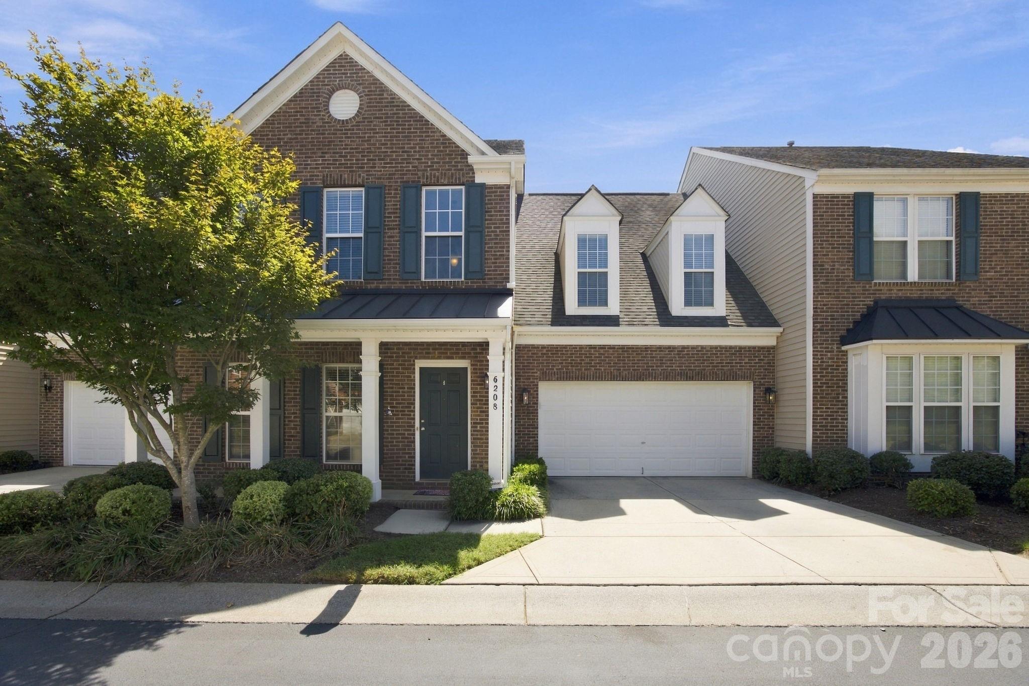 Two-story brick townhouse with dark shutters, a covered entry, and attached double garage.
