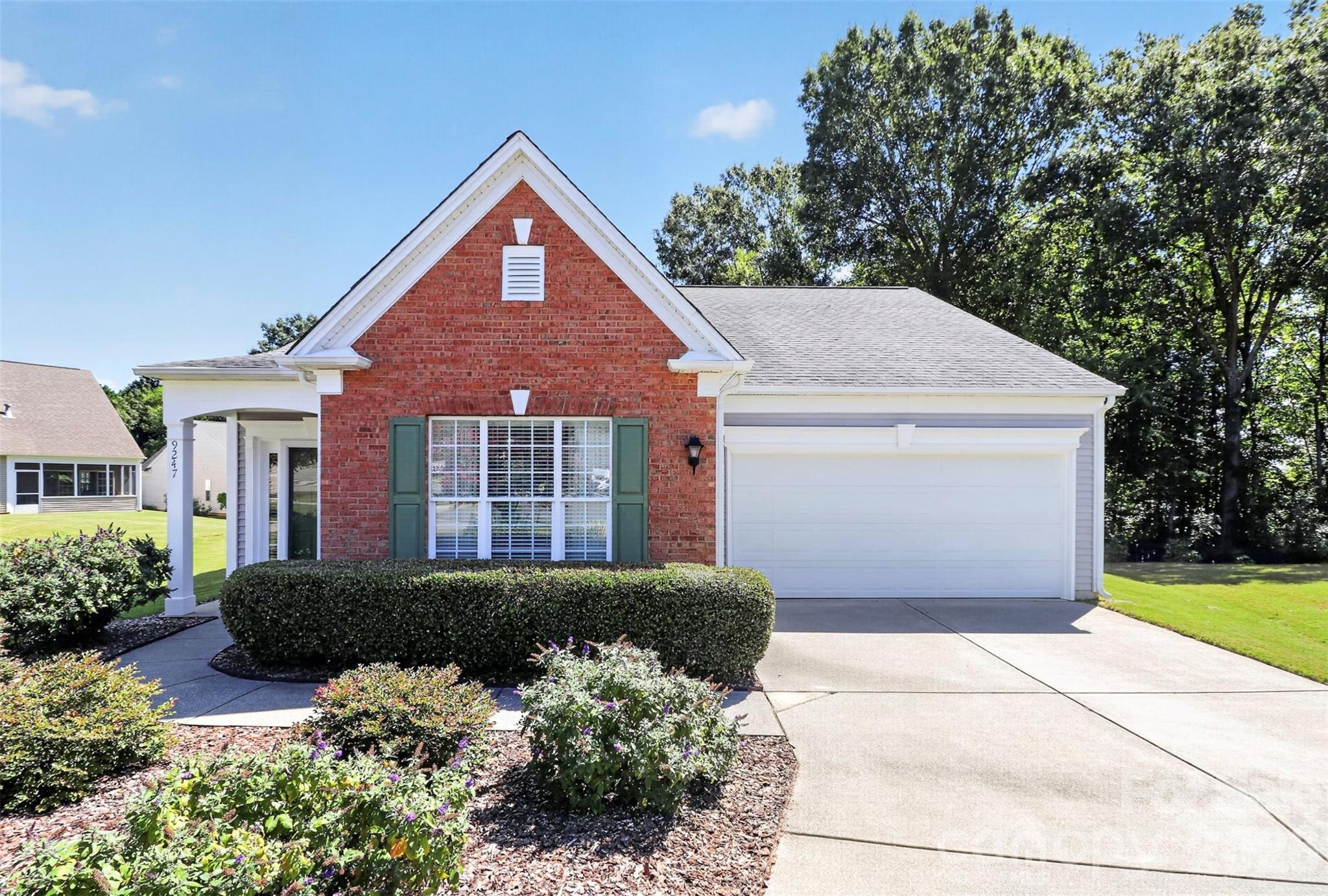 9247 Elrose Place, a red-brick home with green shutters, an attached garage, and landscaped front beds.