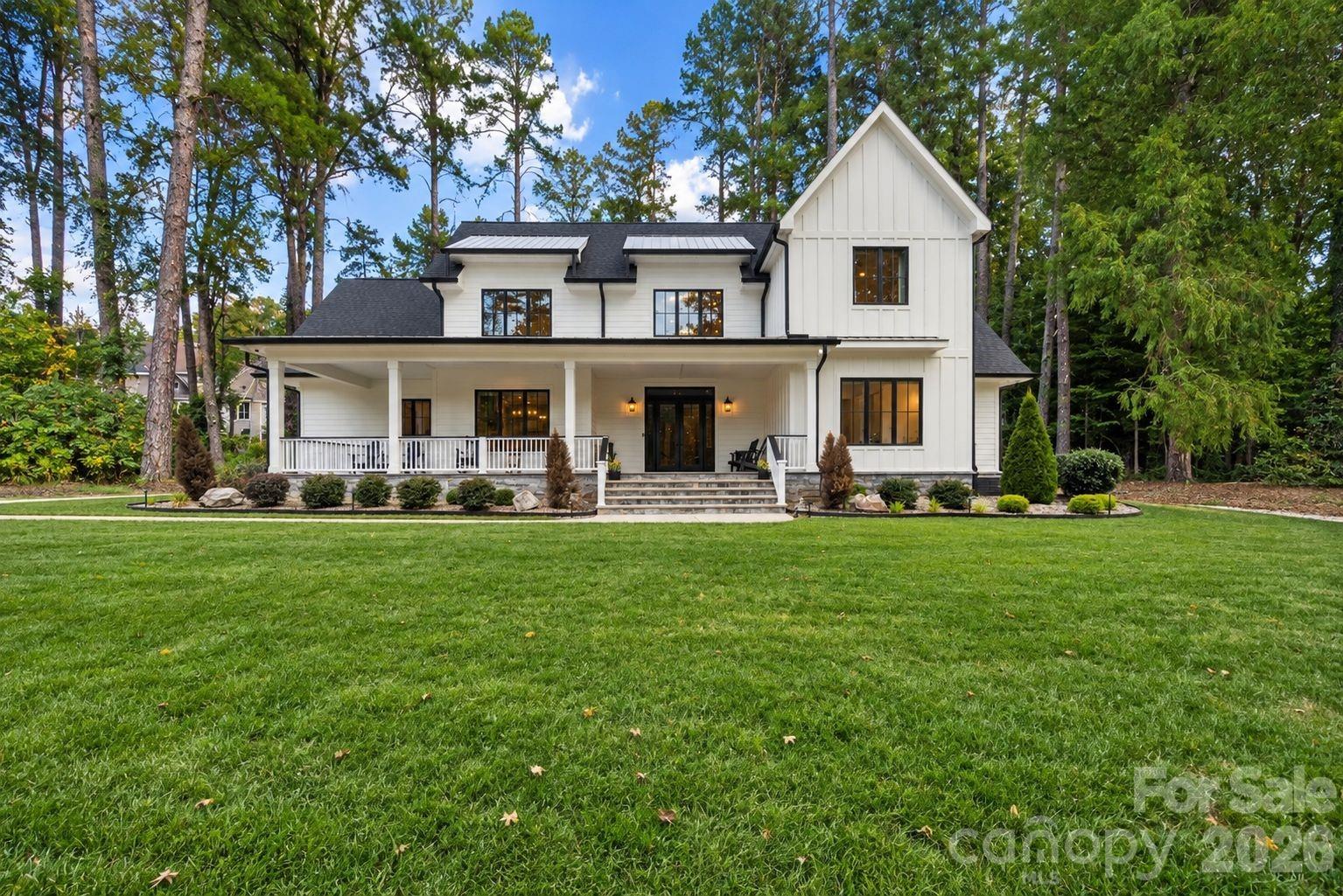 White two-story house with black trim, a covered front porch, and a broad lawn among tall trees.