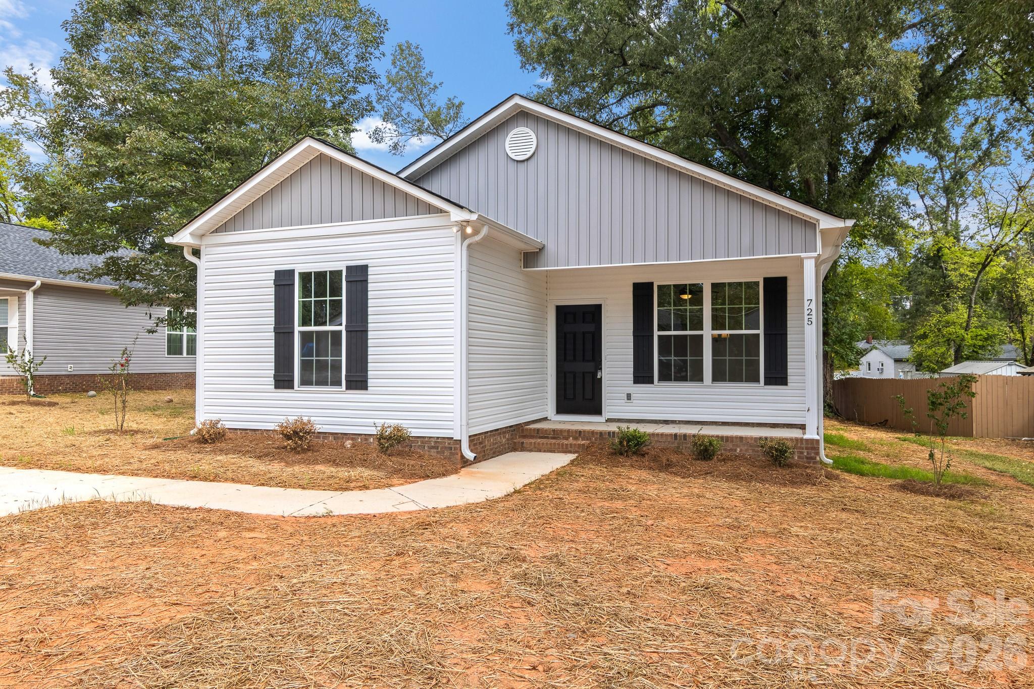 White-sided house with a gray gable, black shutters, and pine-straw front yard.