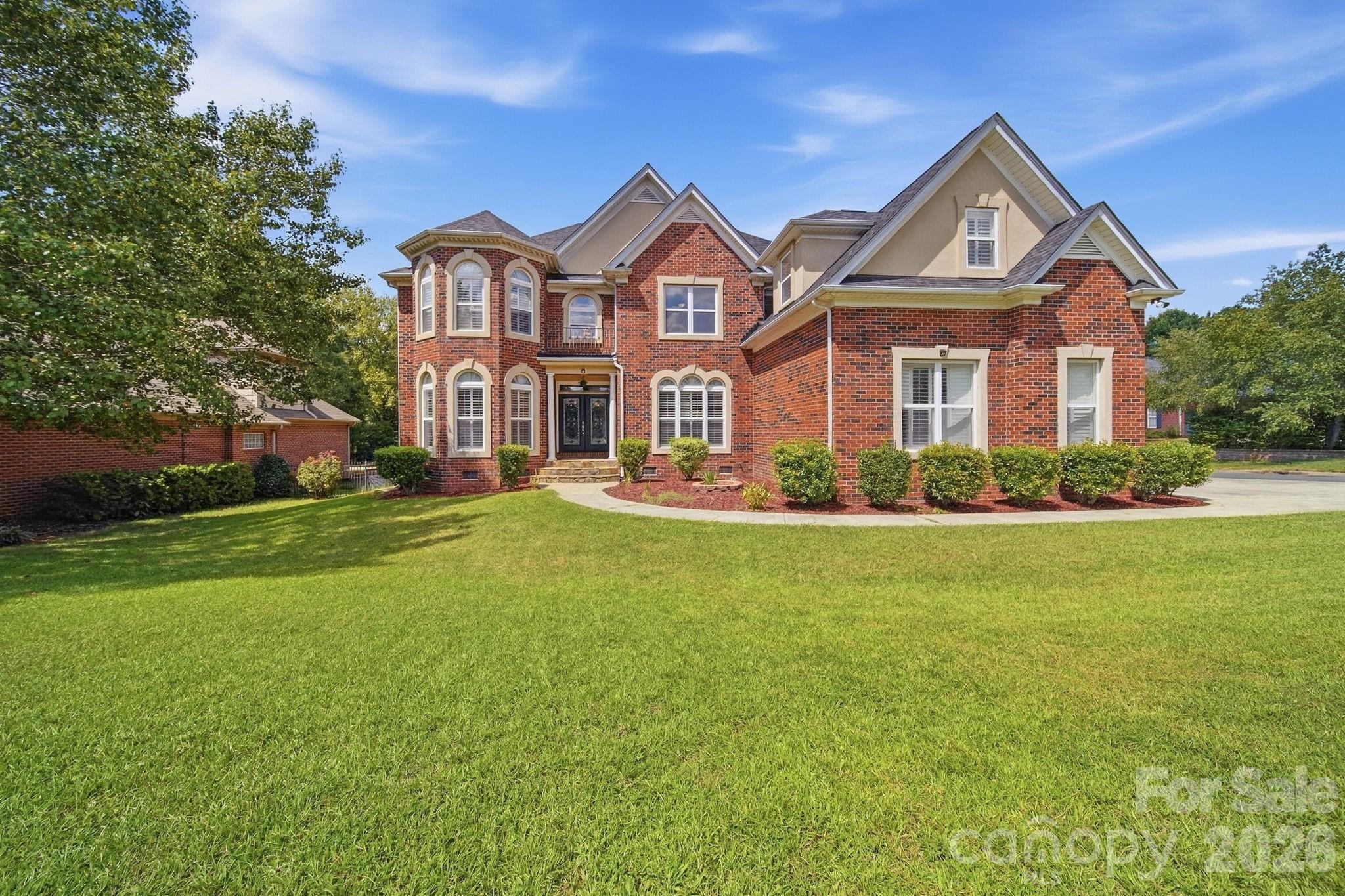 Two-story brick house with tan gables, a rounded bay, and a broad green lawn.