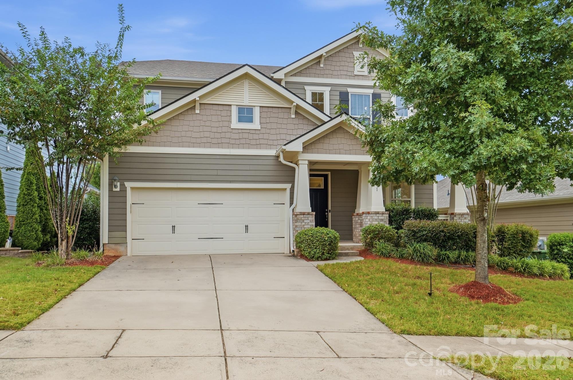 Two-story taupe house with a white double garage, covered entry, and mature trees.