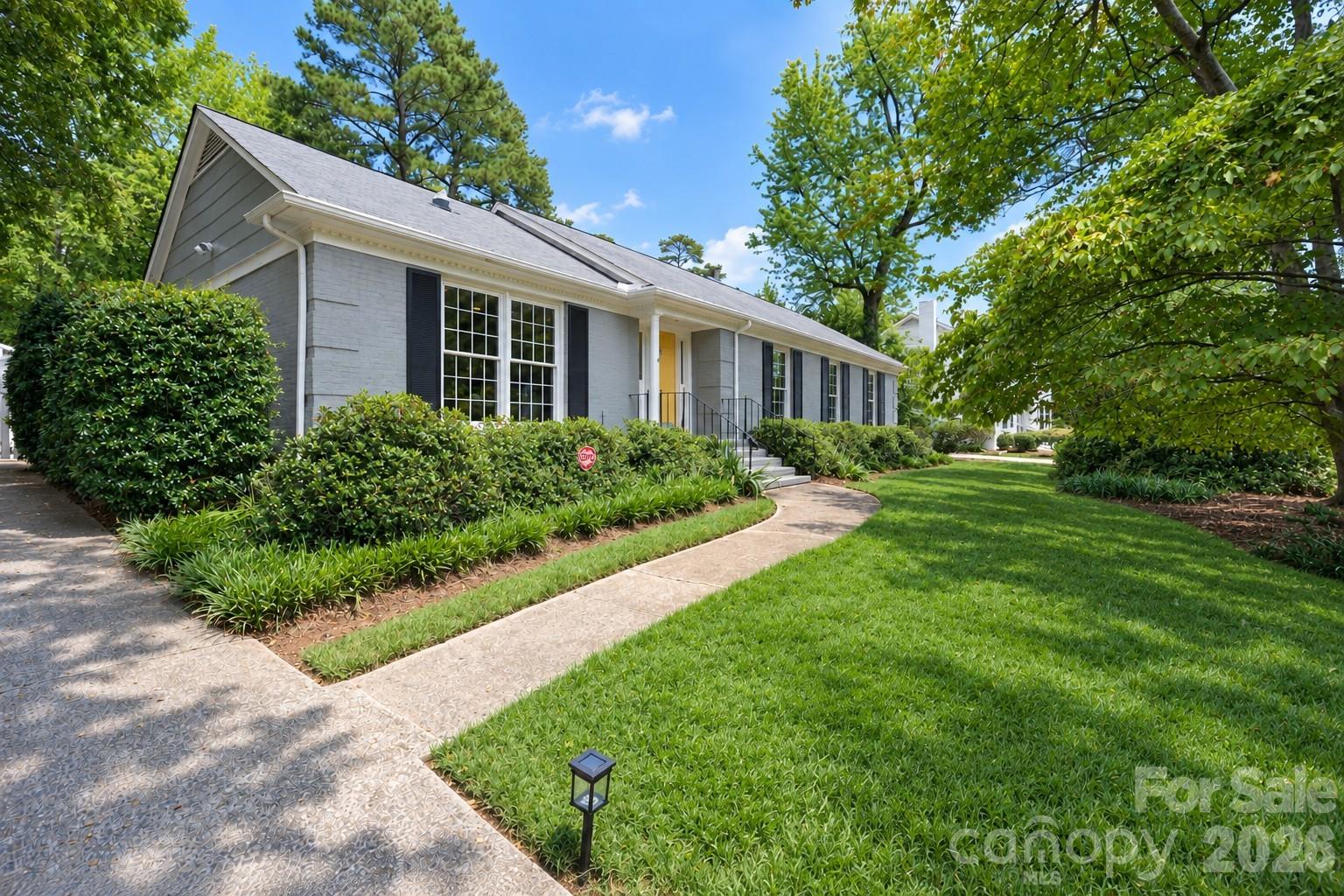 Gray single-story home with dark shutters, a yellow front door, and a curved walkway through landscaped grounds.