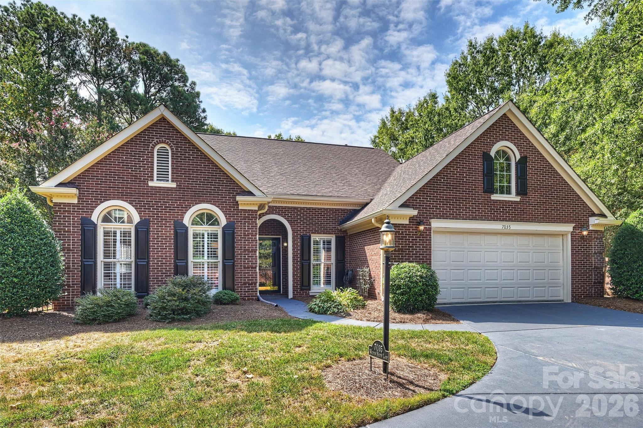 Red-brick house with arched windows, black shutters, and a two-car garage.