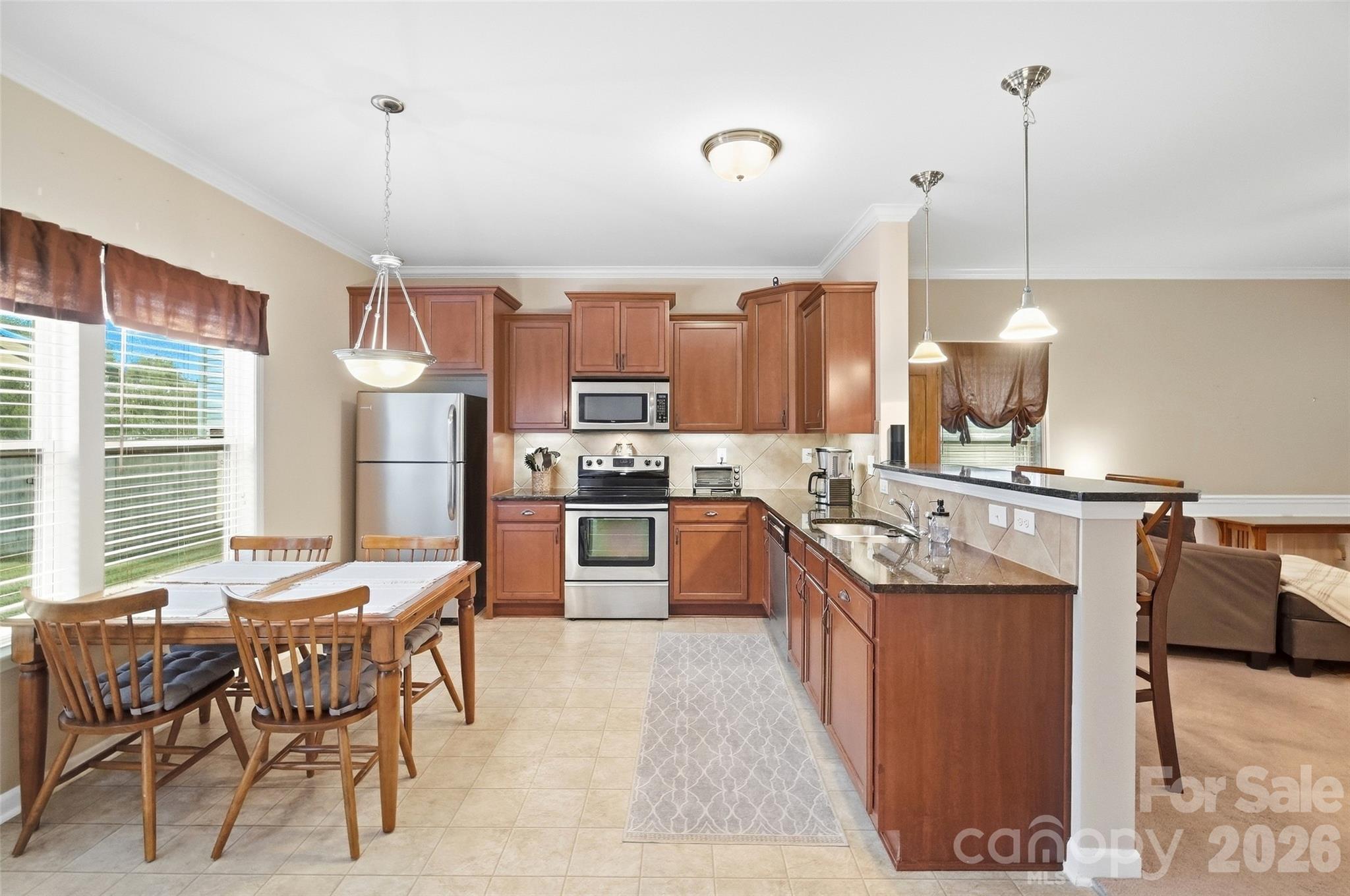 Kitchen with warm wood cabinetry, stainless steel appliances, and a long breakfast bar beside a dining area.
