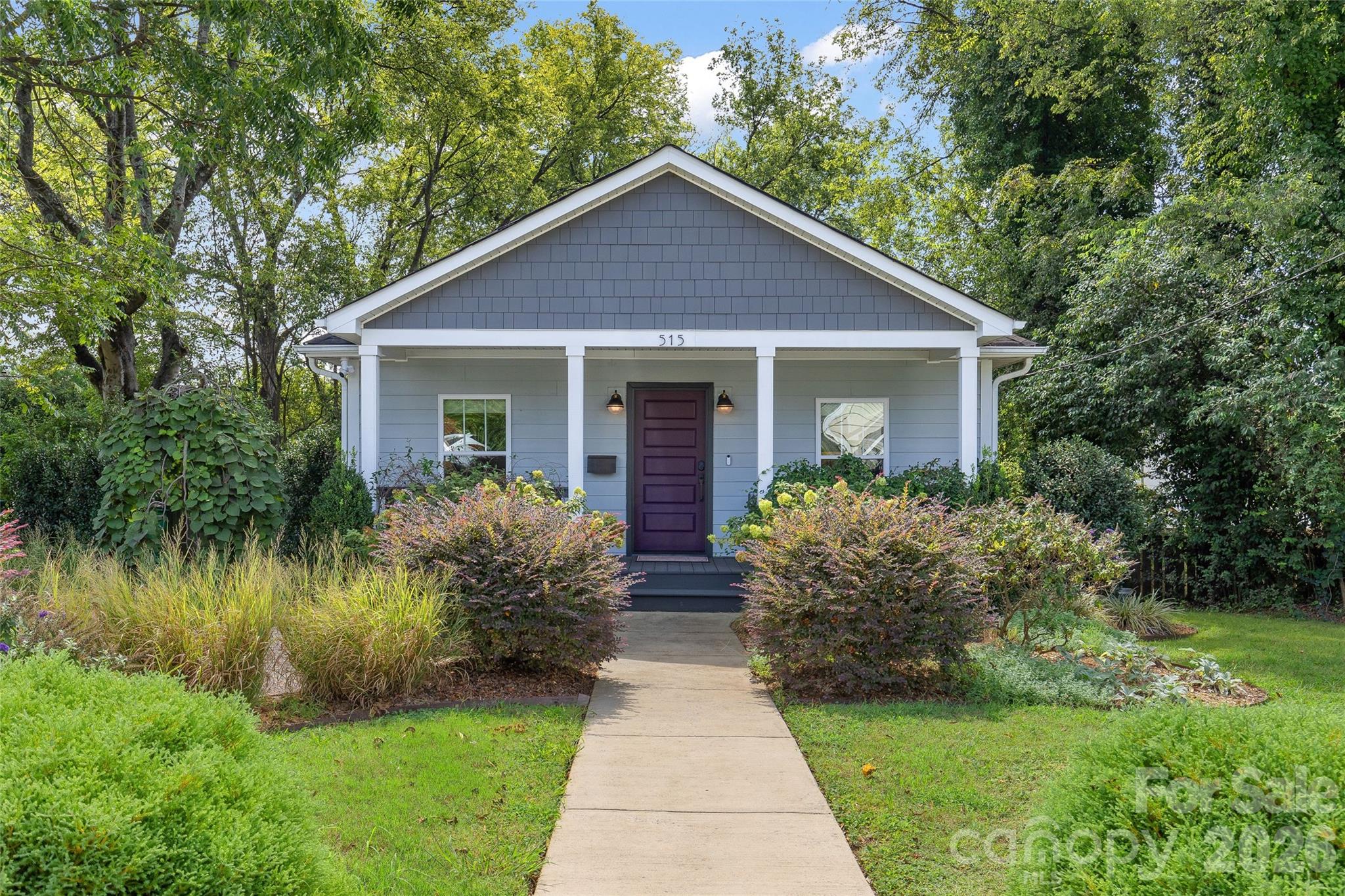 Blue-gray home with white trim, purple front door, and landscaped garden along the walkway.