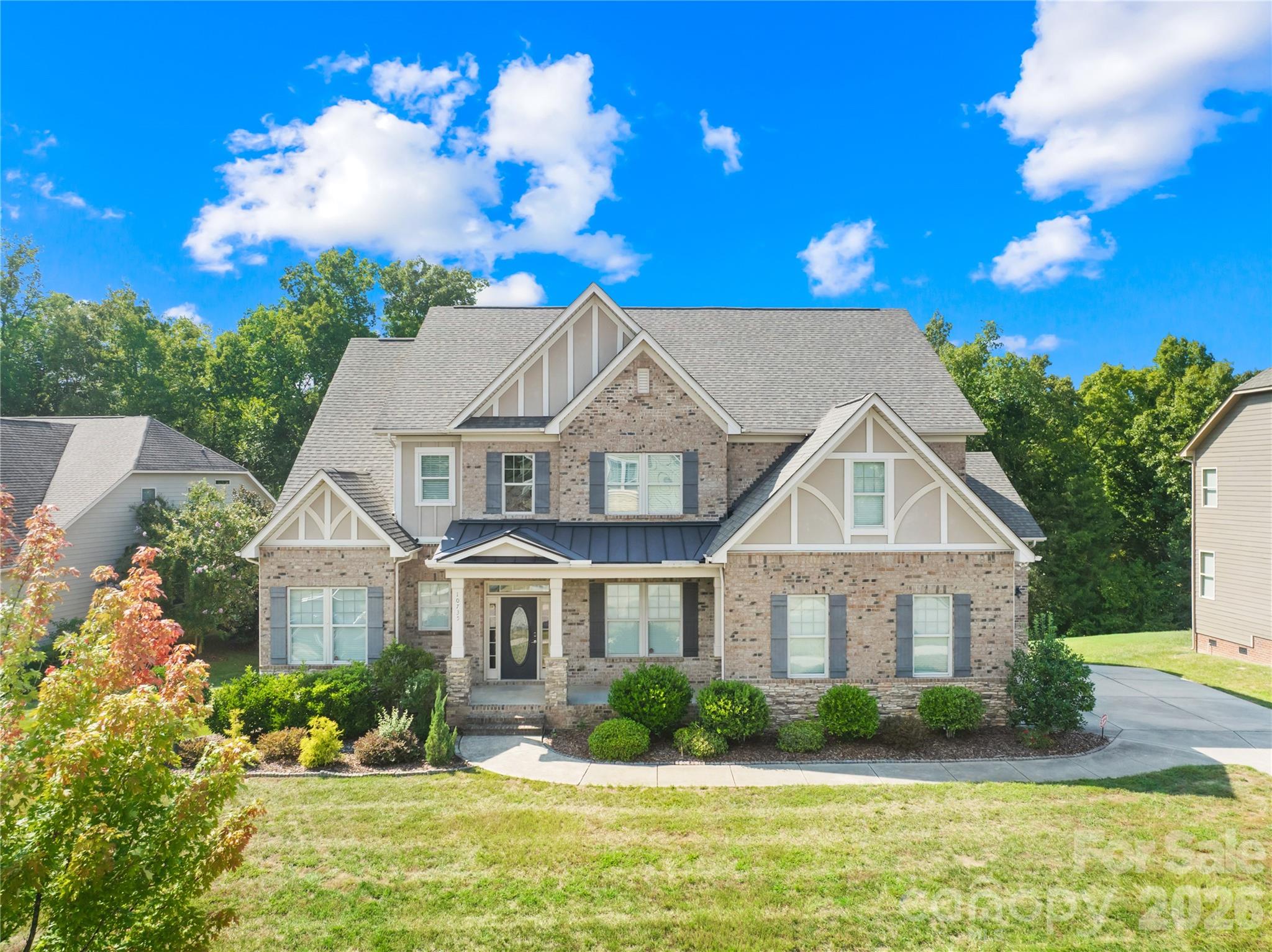 Two-story brick house with front-facing gables, gray shutters, and a landscaped yard.