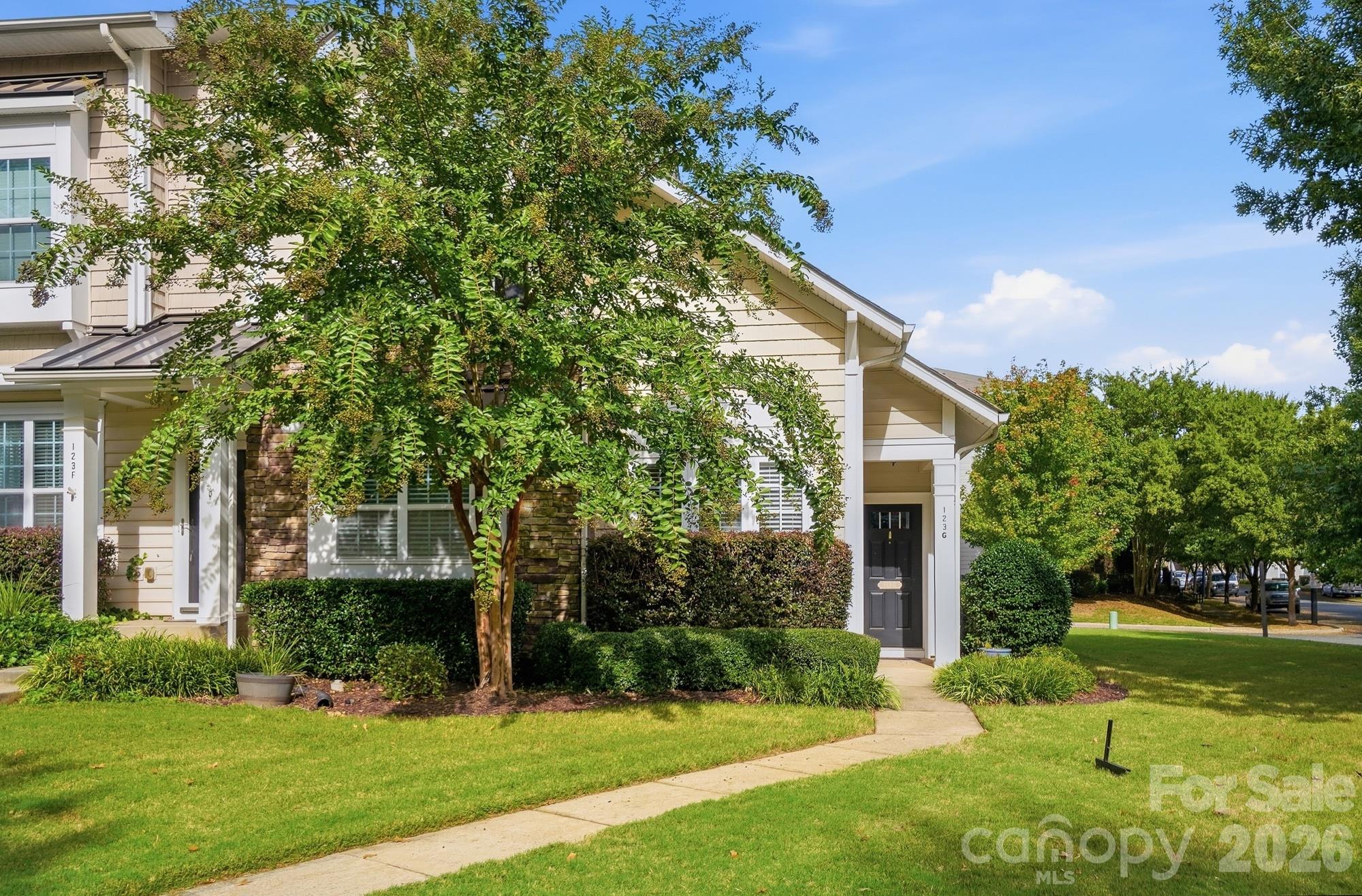 Beige attached home with stone accents and a landscaped front lawn beneath mature trees.