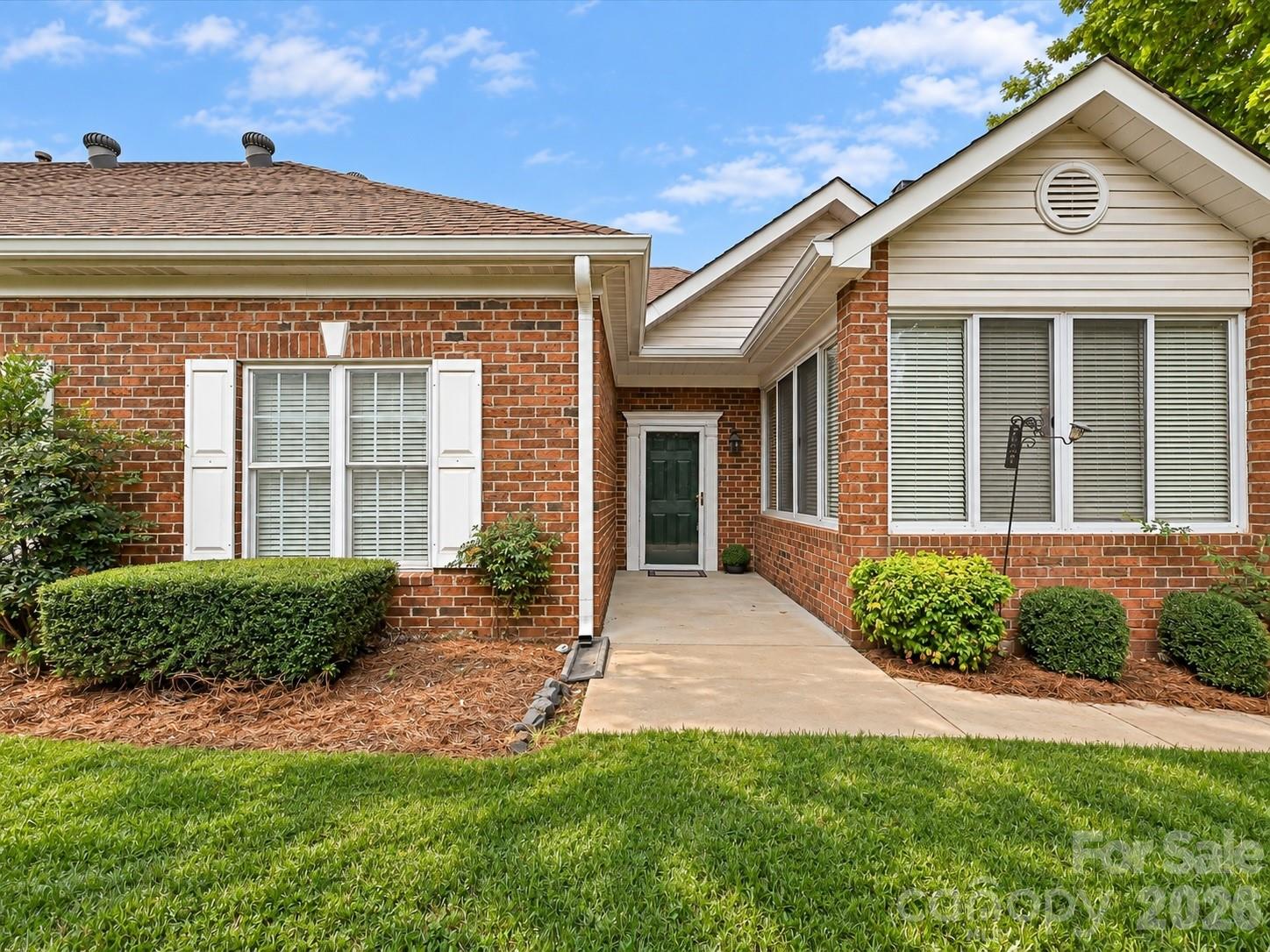 Red brick home with a recessed entry, white shutters, and a neatly landscaped front lawn.