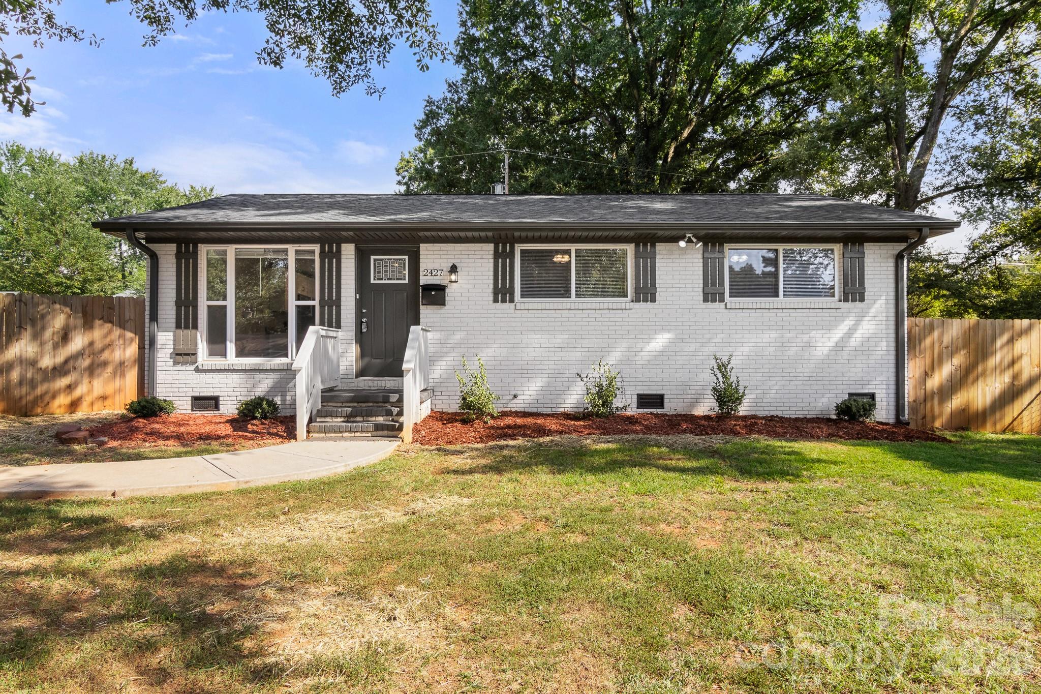 White brick single-story home with dark trim, front steps, and a fenced lawn.