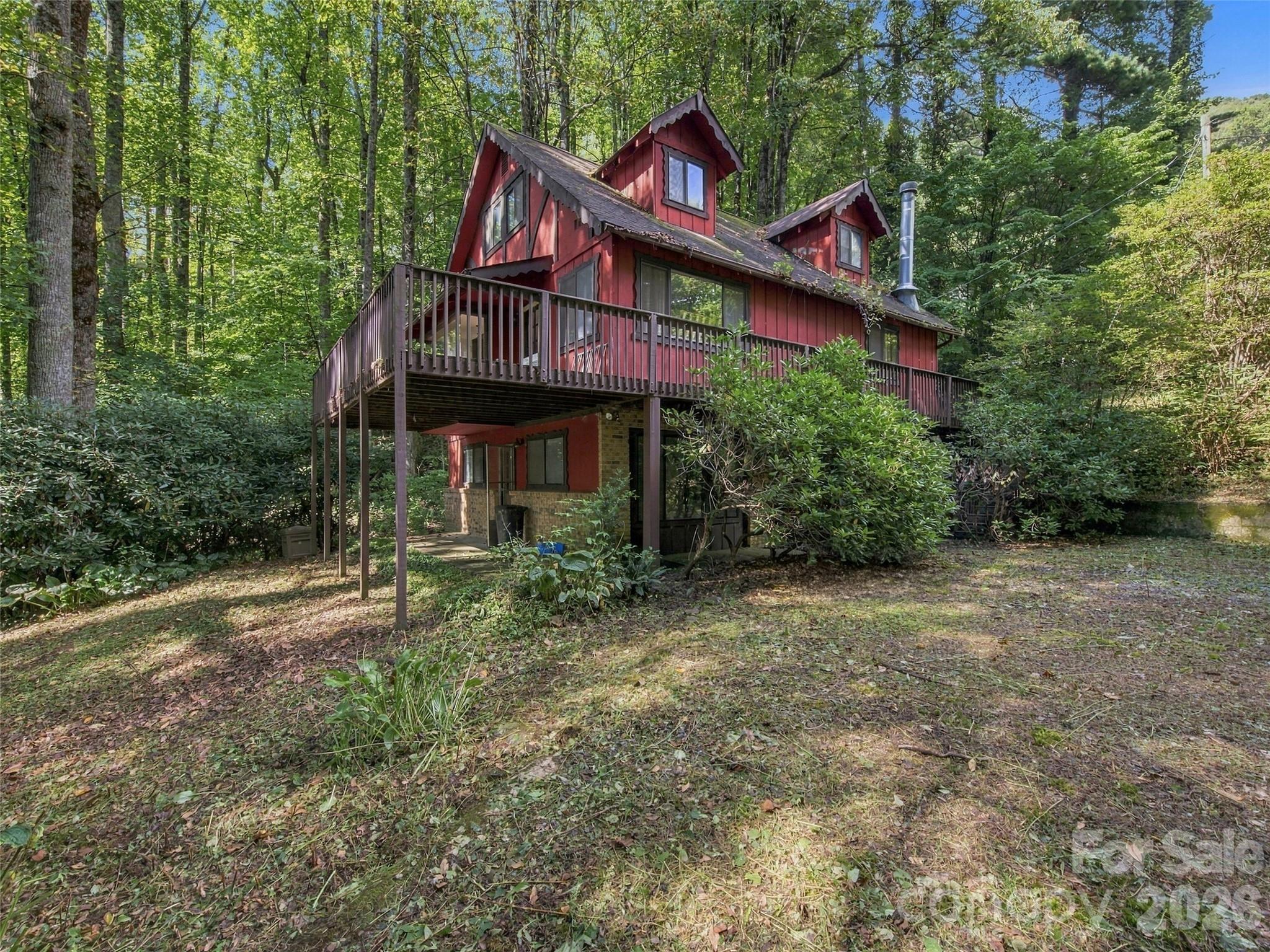 Red wooded cabin with a large elevated deck surrounded by trees.