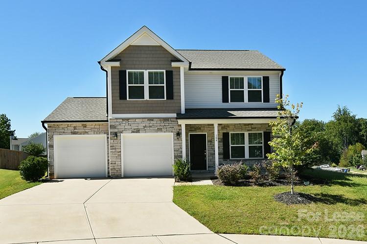 Two-story gray house with stone accents, two garage doors, and a wide driveway.