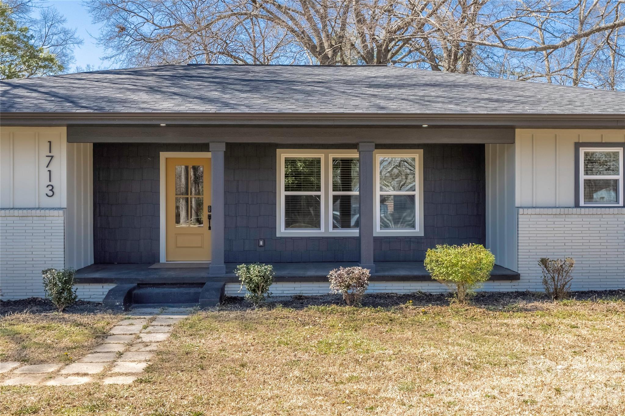 Single-story home with dark blue siding, white brick accents, and a mustard-yellow front door.