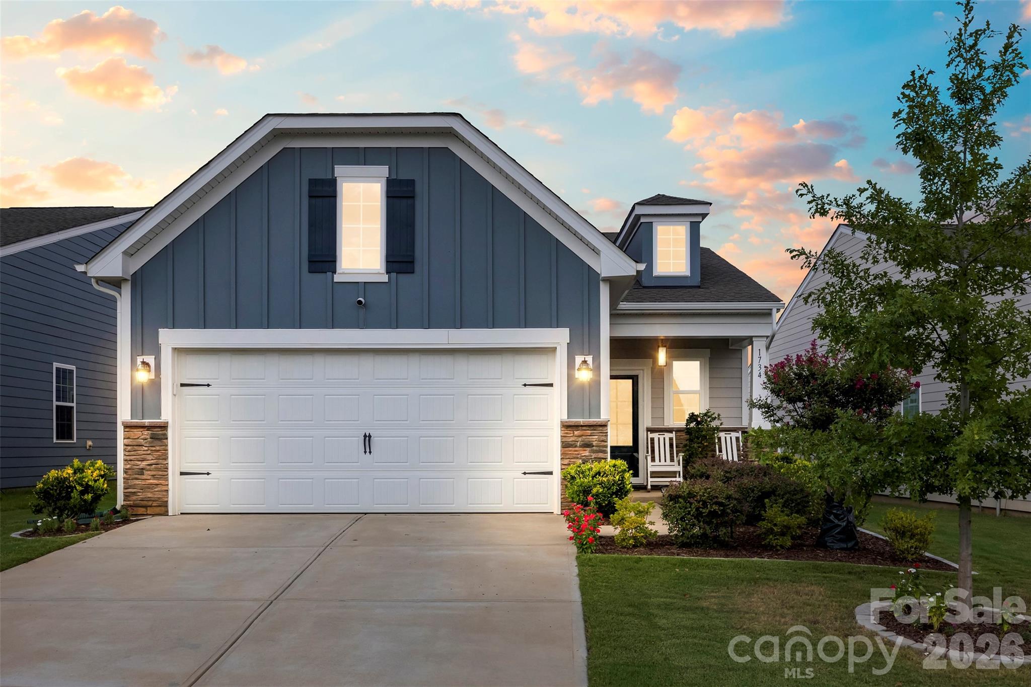 Blue-gray two-story house with a white double garage and landscaped front yard at sunset.