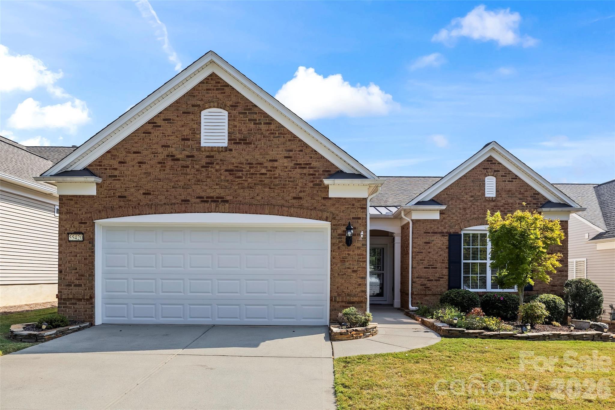 Brick house with a white double garage, landscaped front garden, and house number 55420.