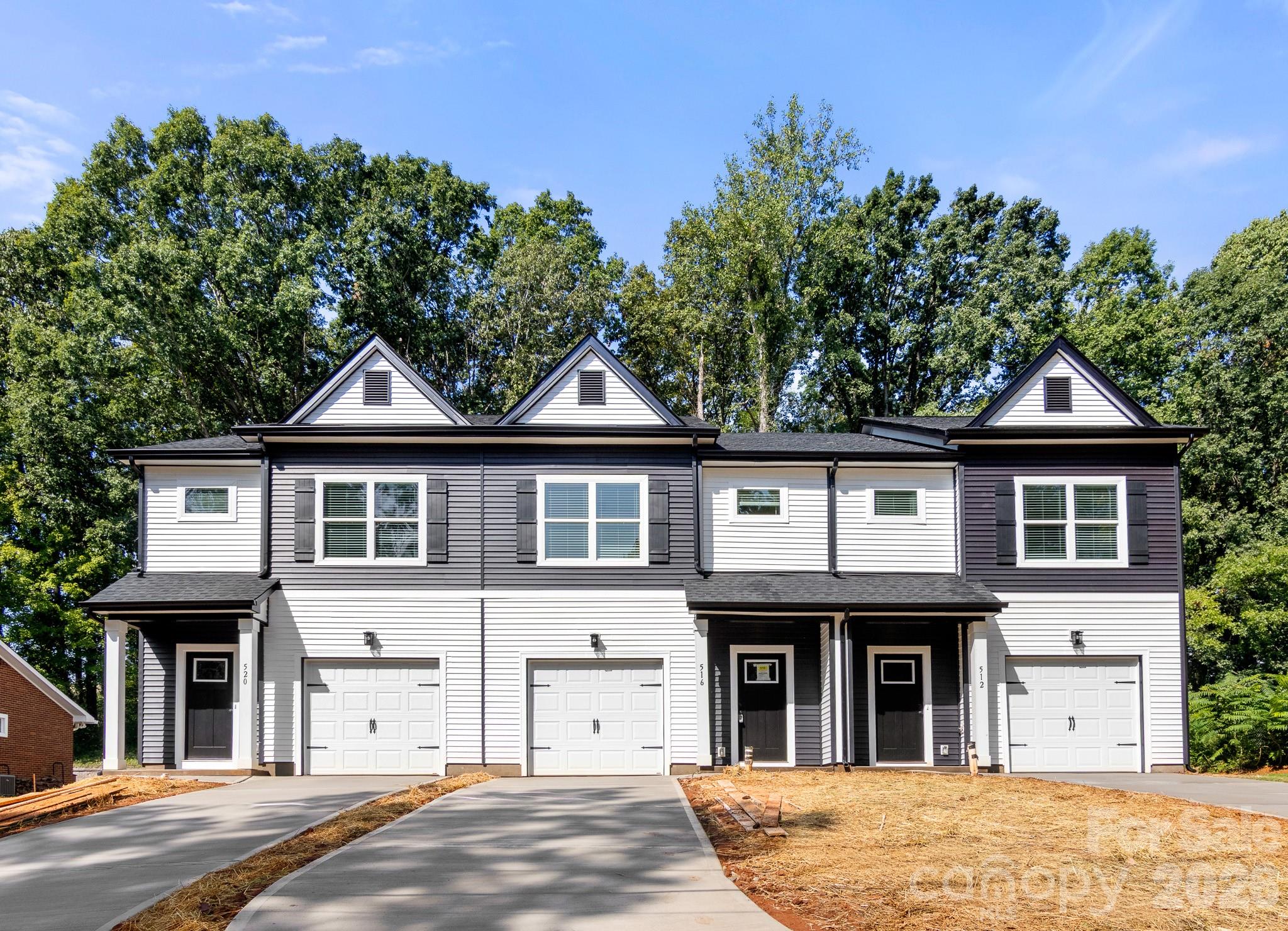 Three attached gray-and-white townhomes with front-entry garages and unfinished yards.