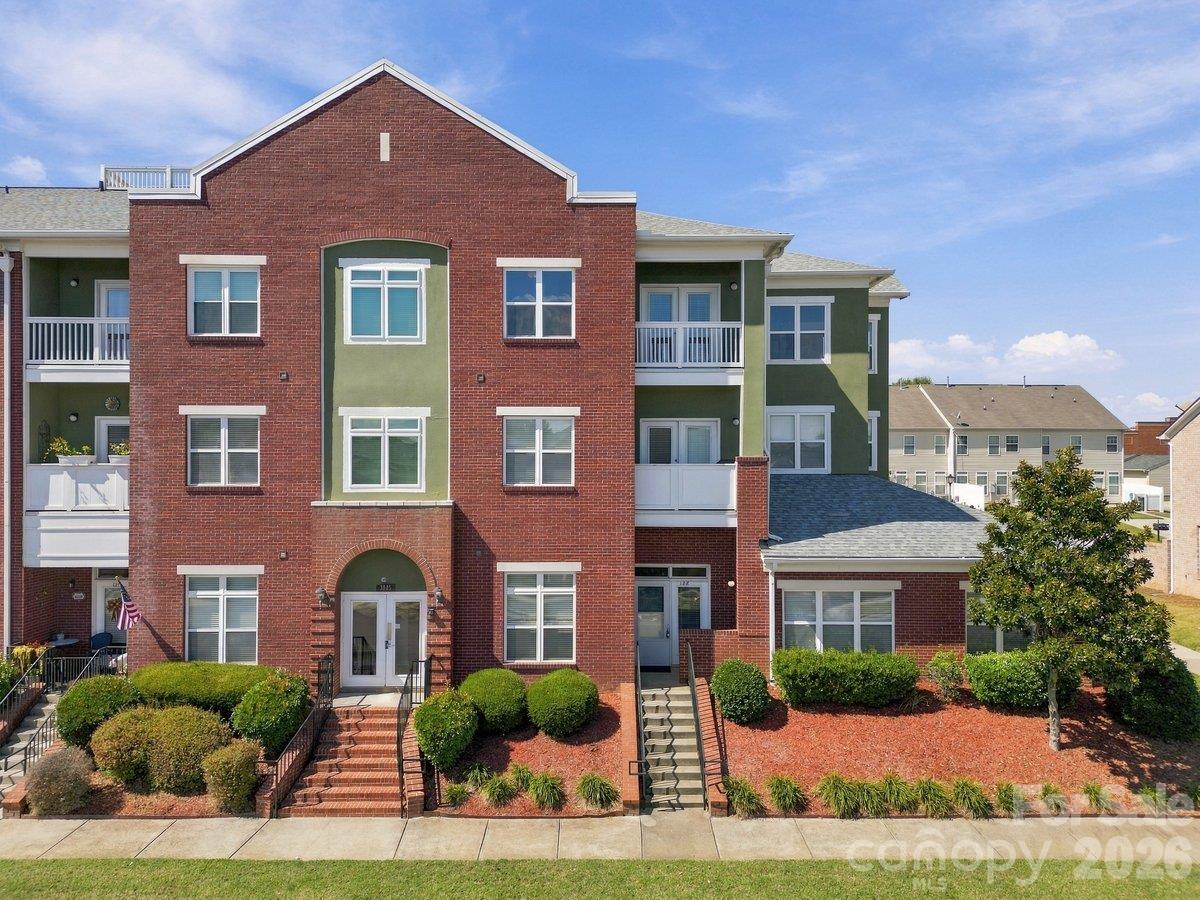 Multi-unit residential building with a red brick facade, green siding, white balconies, and landscaped front entrance.