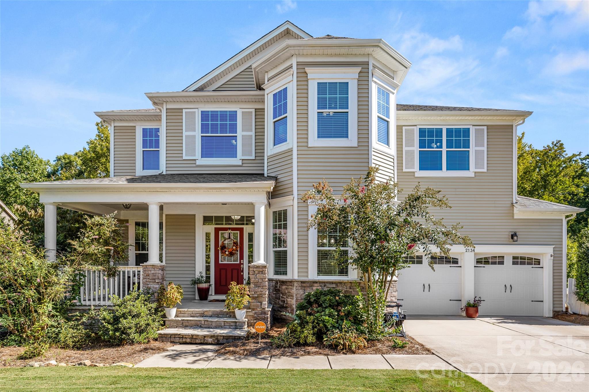 Two-story beige house at 2134 Clarion Drive with a red front door, covered porch, and attached two-car garage.