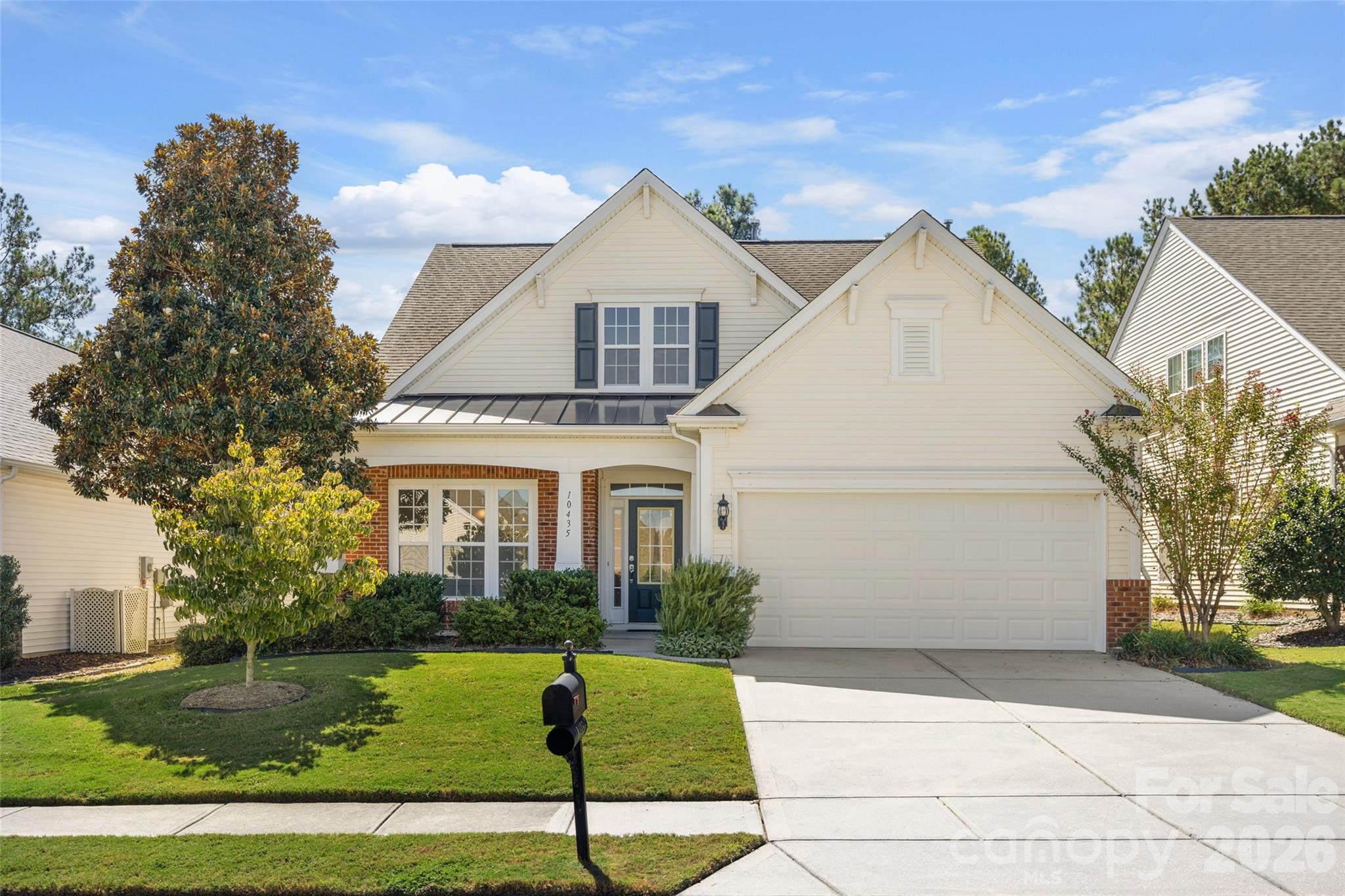 Cream two-story house with brick accents, dark shutters, attached garage, and landscaped front lawn.
