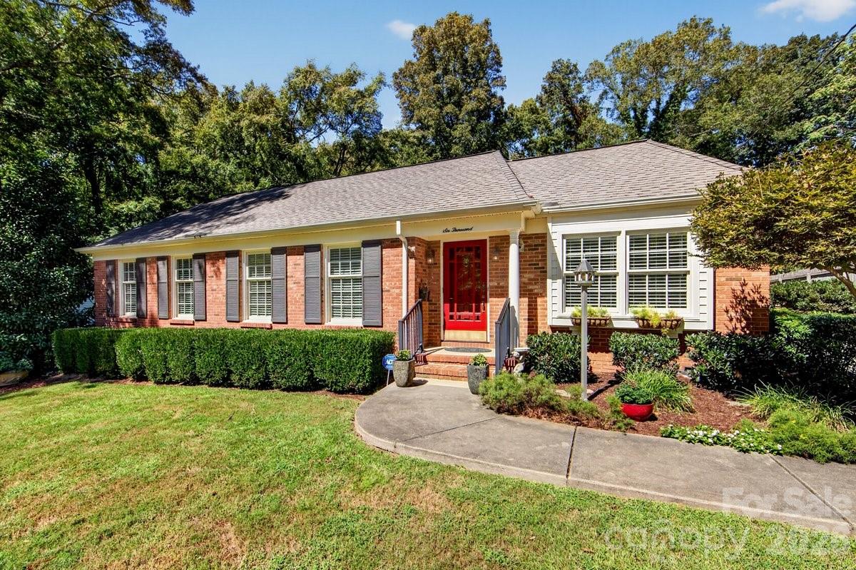 Single-story brick house with a red front door, curved walkway, and landscaped lawn.